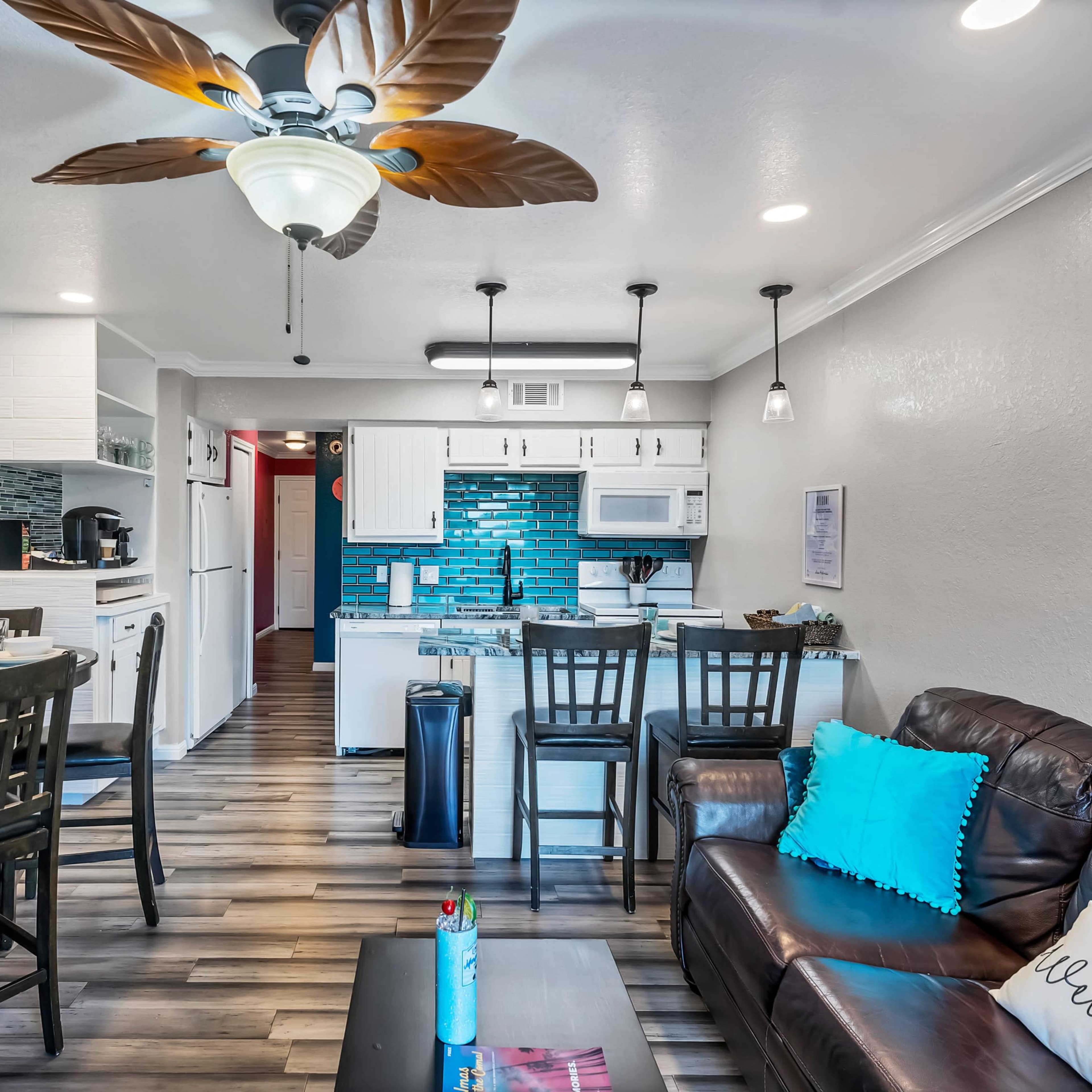 A modern living space featuring a kitchen, dining area, and comfortable seating with vibrant wall decor and wooden flooring.