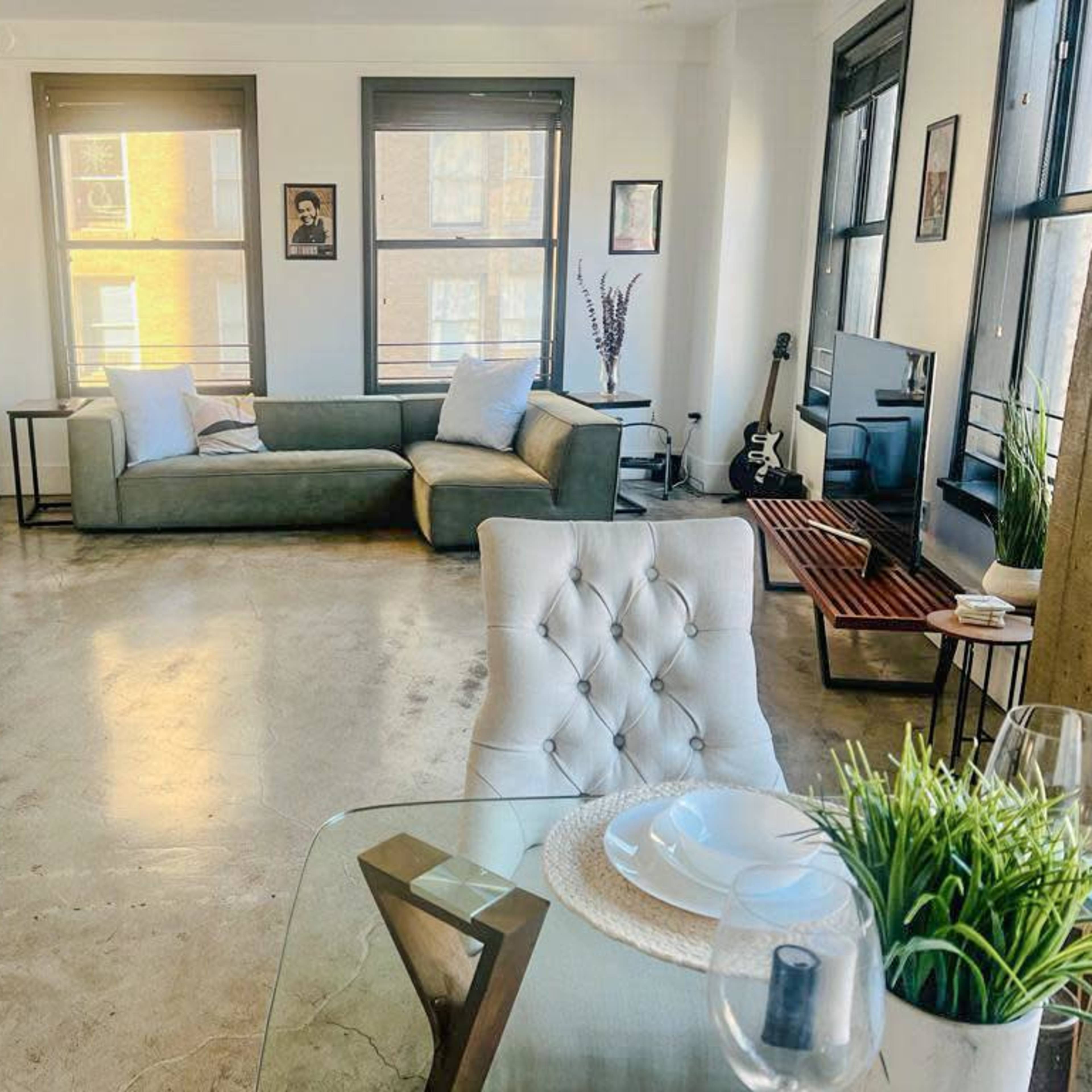 A modern living space with a sectional sofa, dining table, and decorative elements, featuring large windows that allow natural light to fill the room.
