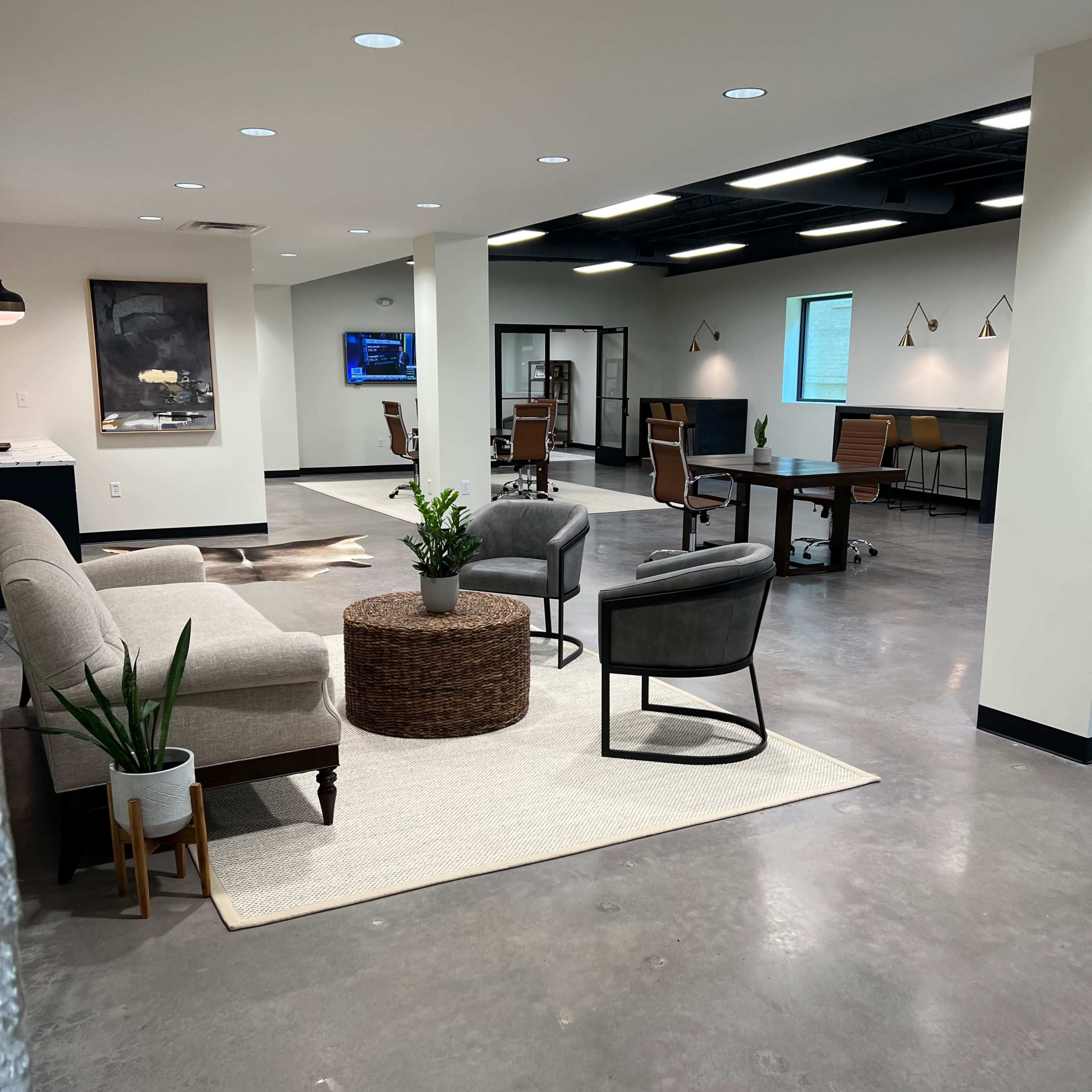 A modern office space with a seating area featuring gray chairs, a round table, and a rug, alongside workstations equipped with chairs and computers.