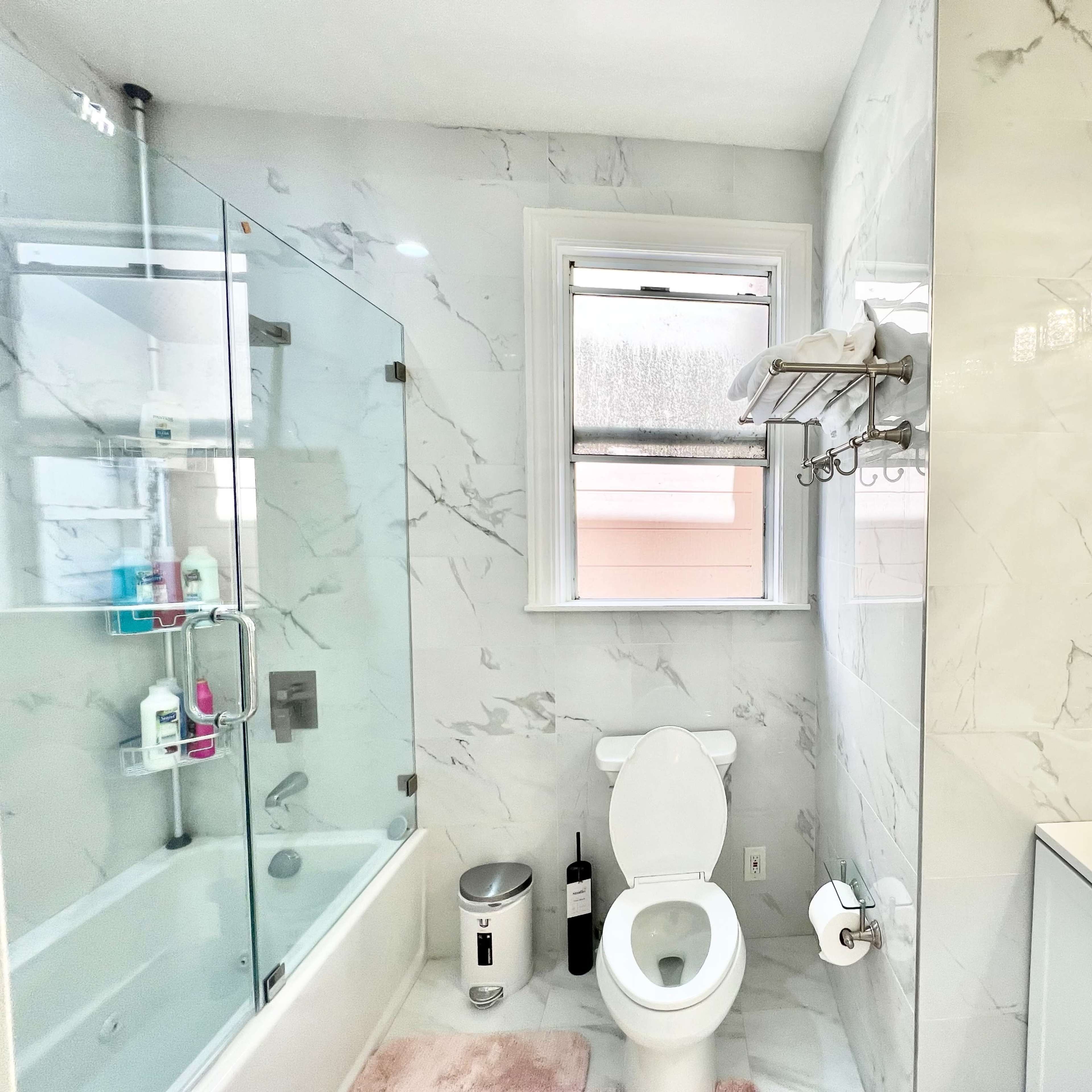 A modern bathroom featuring a glass shower, a white toilet, a sink with a mirror, and marble-patterned walls.
