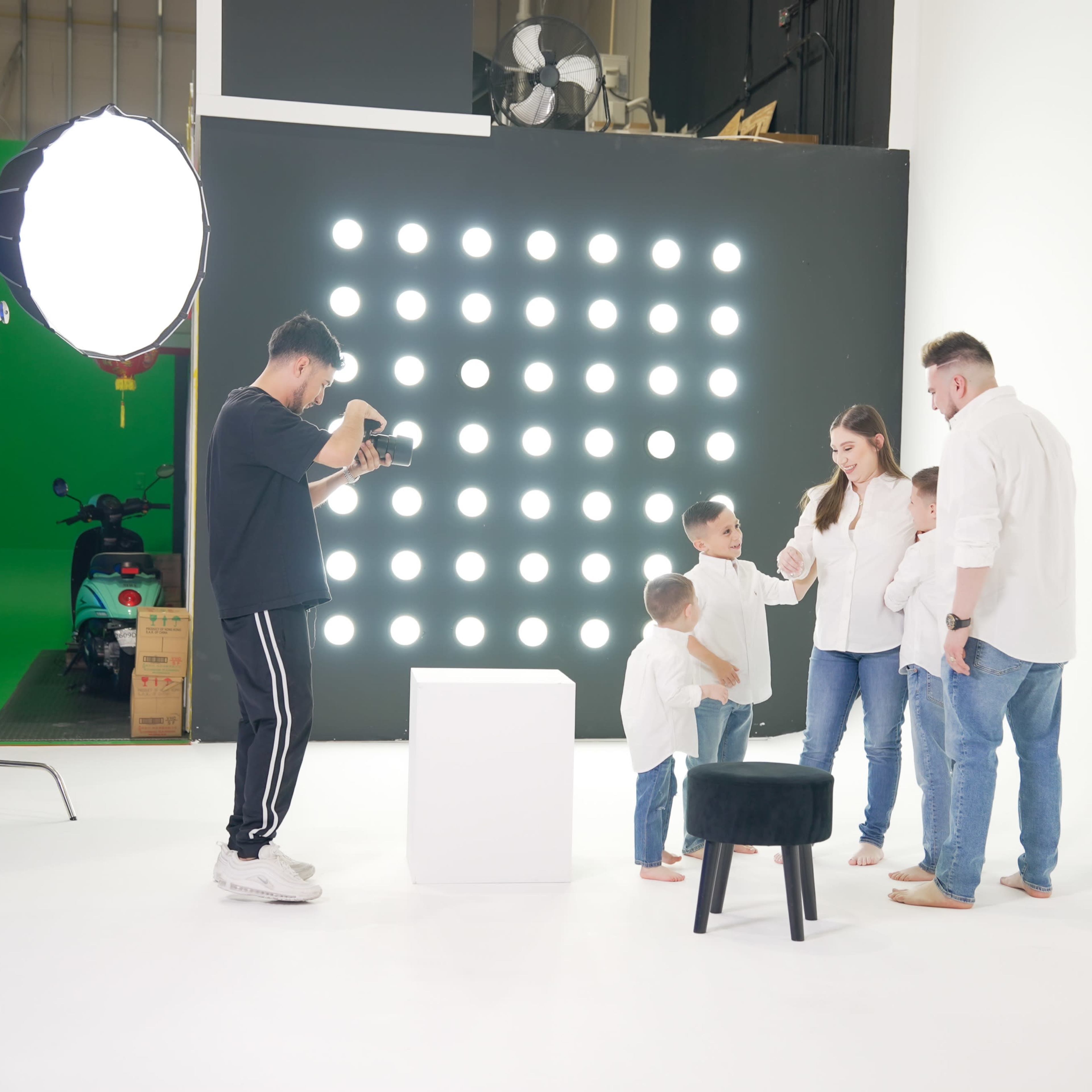 A photographer captures a family interacting in a studio setting with bright lights and a minimalist background.