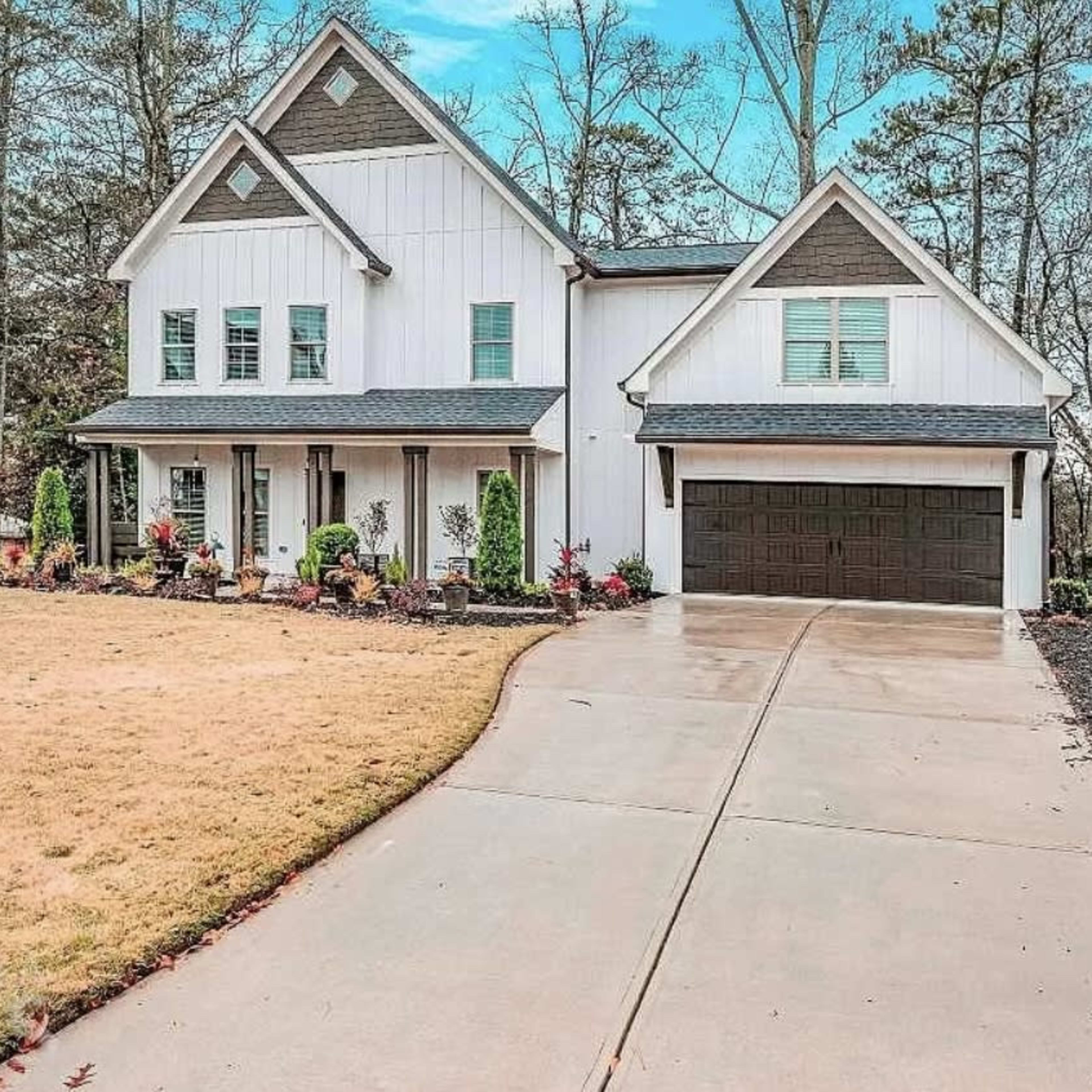 A white two-story house with a gray roof features a spacious driveway and landscaped front yard.