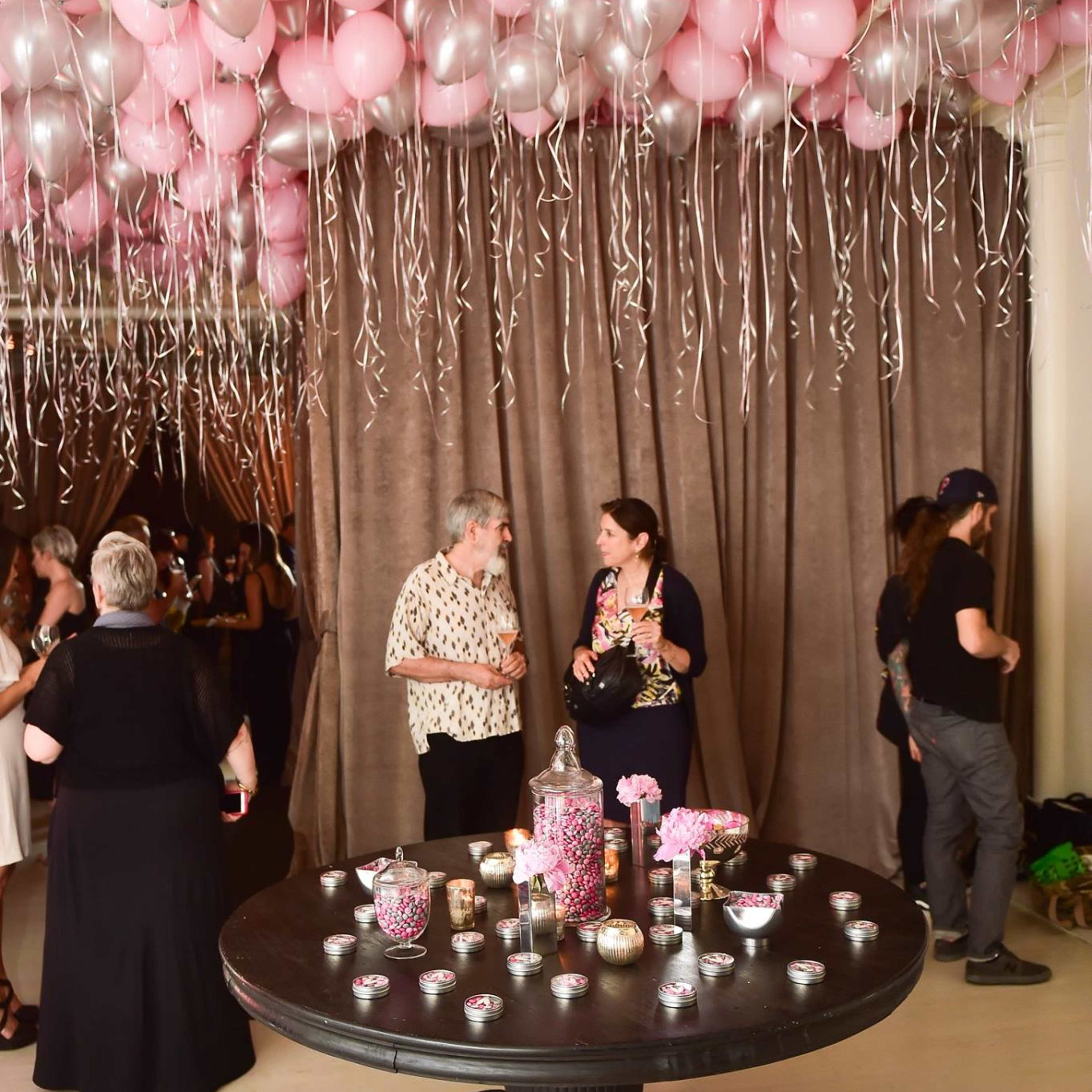 A black table covered with various decorative items sits in a room with a ceiling adorned with pink balloons and glittering streamers.