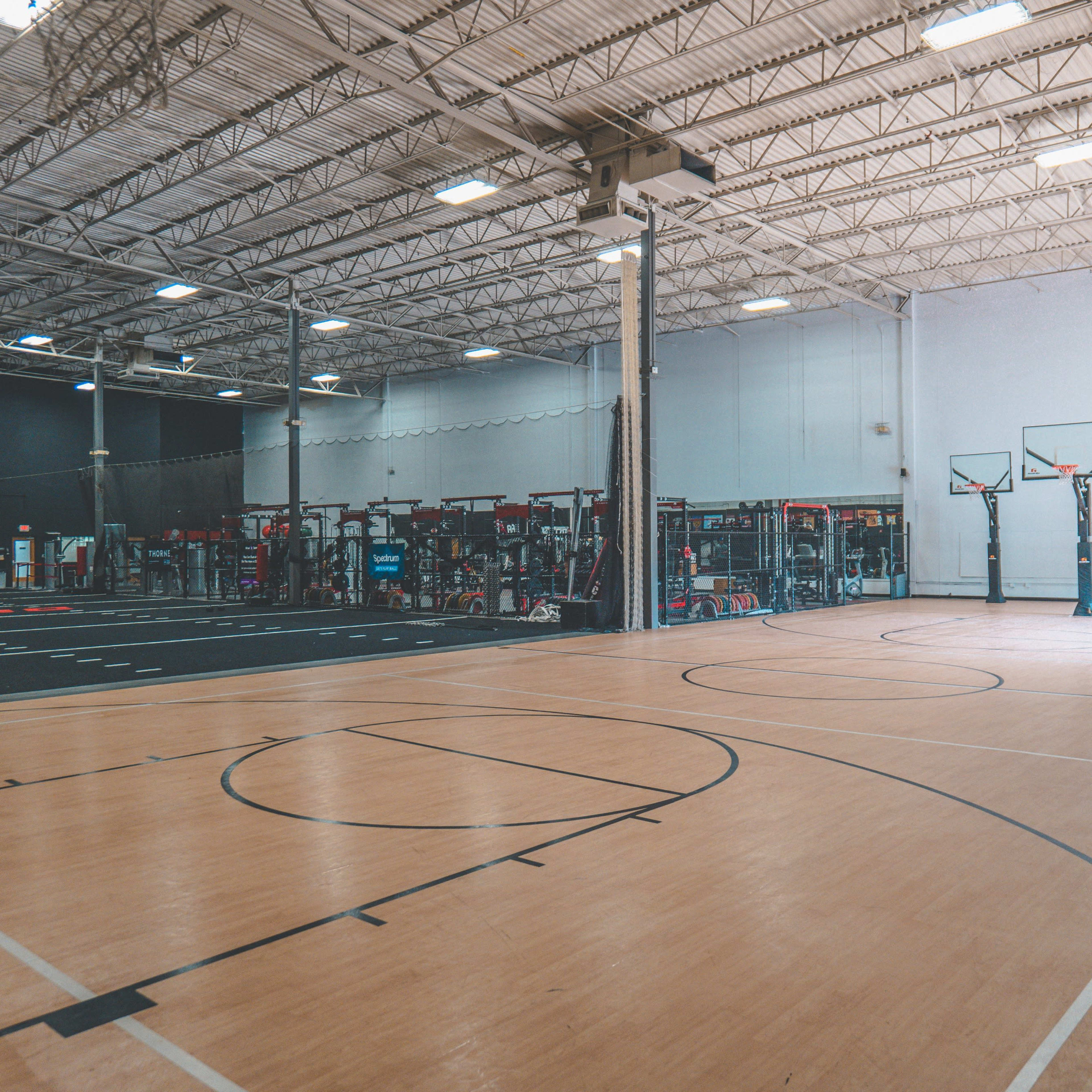 An indoor basketball court with multiple hoops and adjacent workout equipment areas.