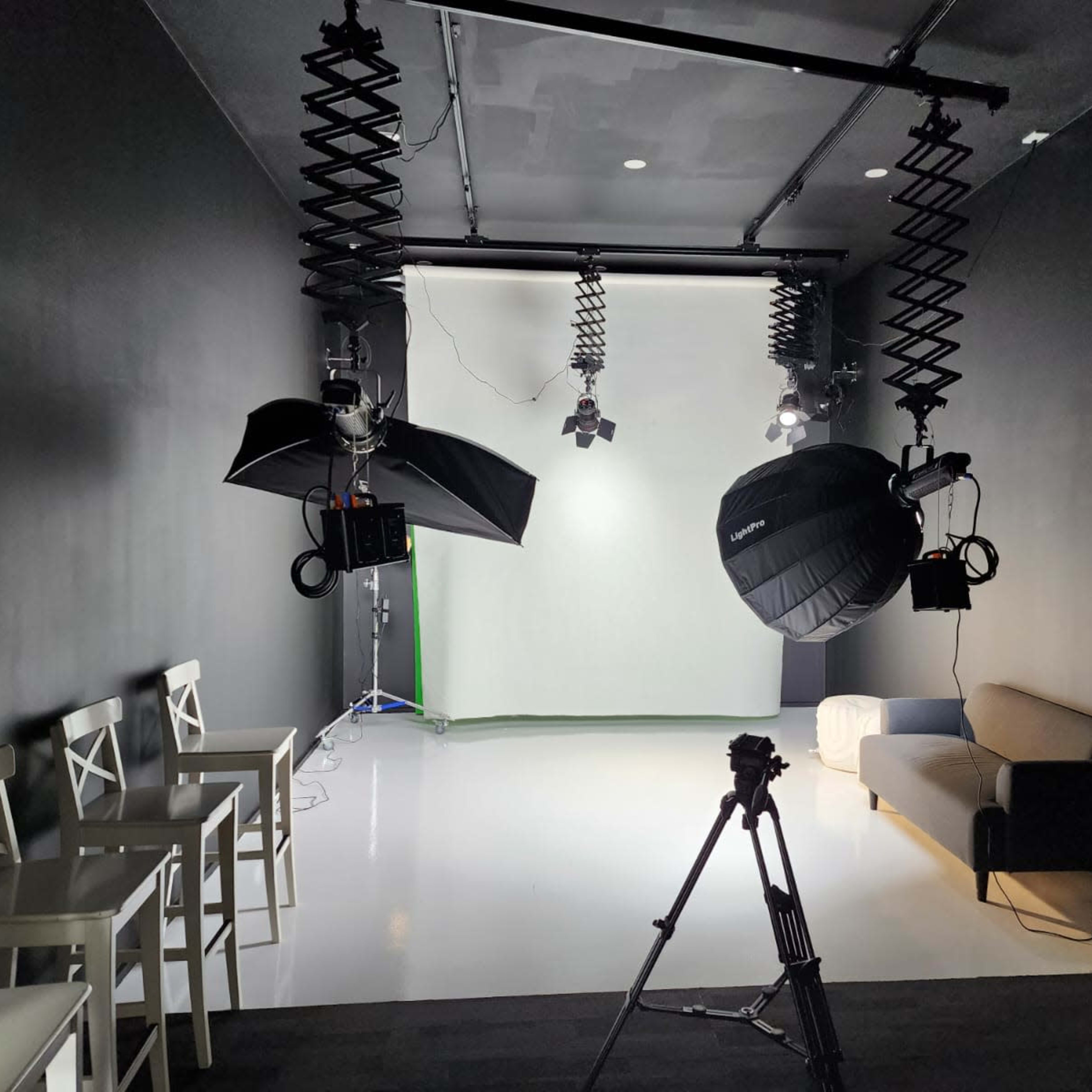 A photography studio is set up with a seamless backdrop, lighting equipment, and a tripod, alongside chairs and a sofa.
