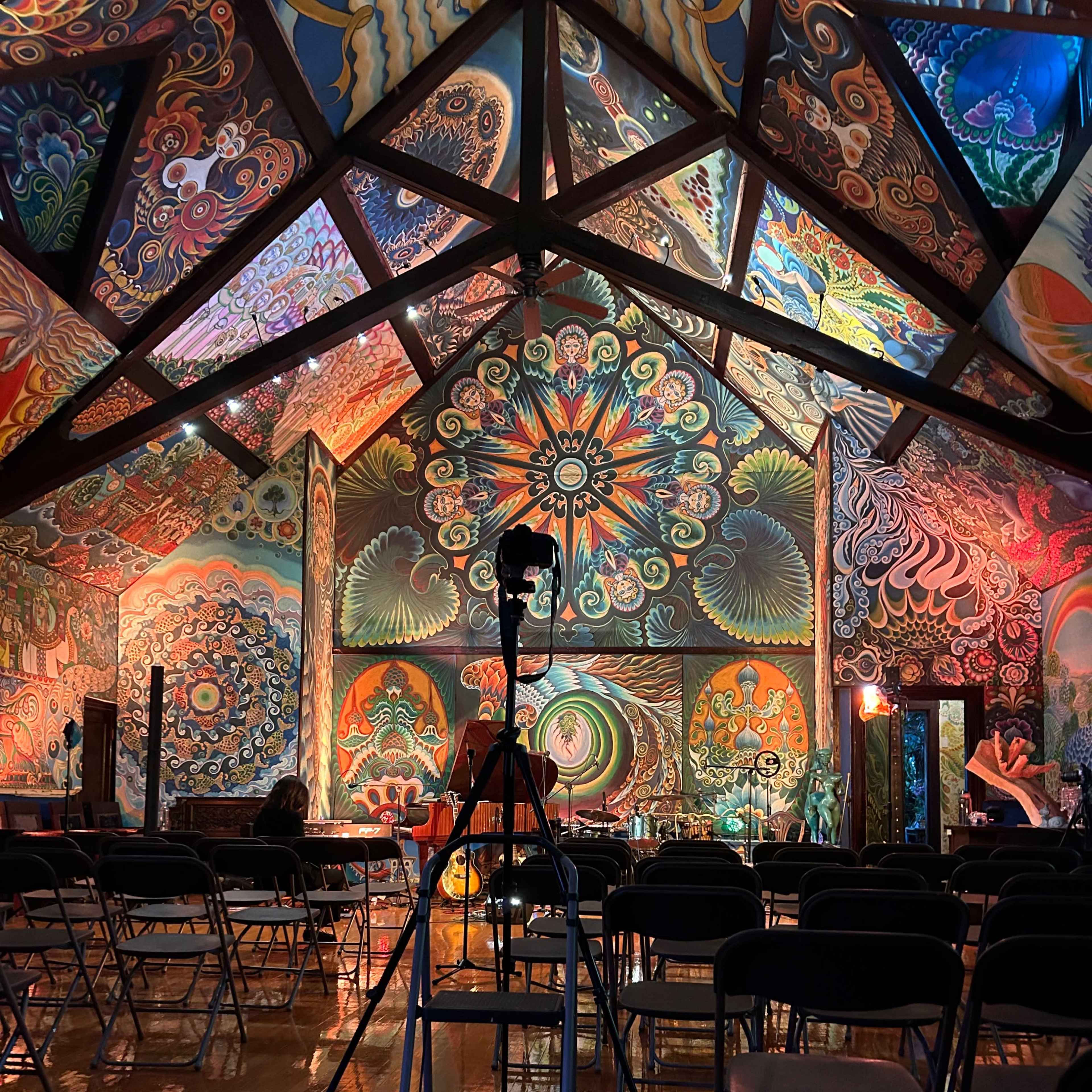 A vibrant mural-covered room with a tripod positioned in front of empty folding chairs.