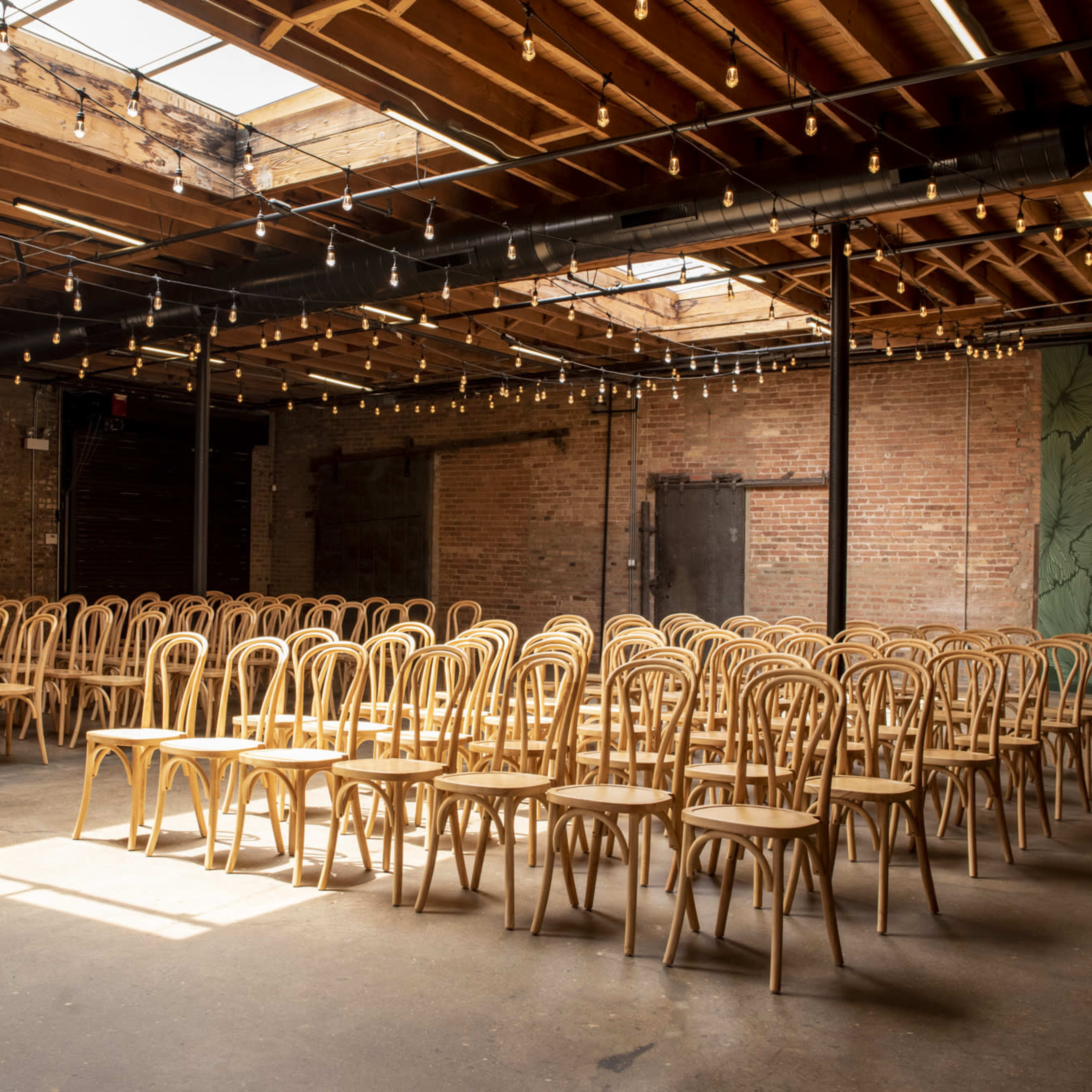A spacious room filled with rows of wooden chairs under a ceiling adorned with string lights.
