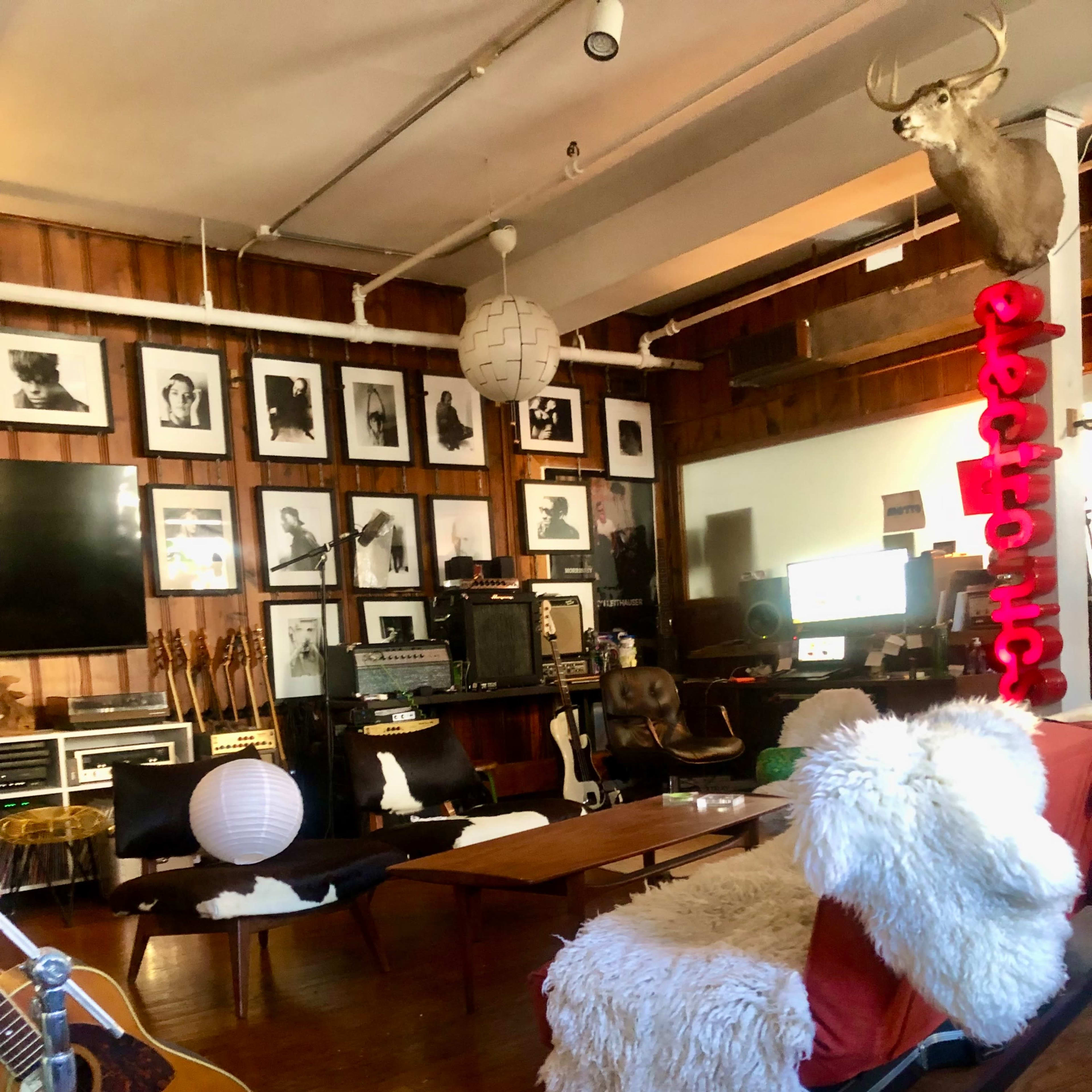 The room features a cozy seating area with a white fur throw, musical instruments, framed photographs on the wooden walls, and a vintage television setup.