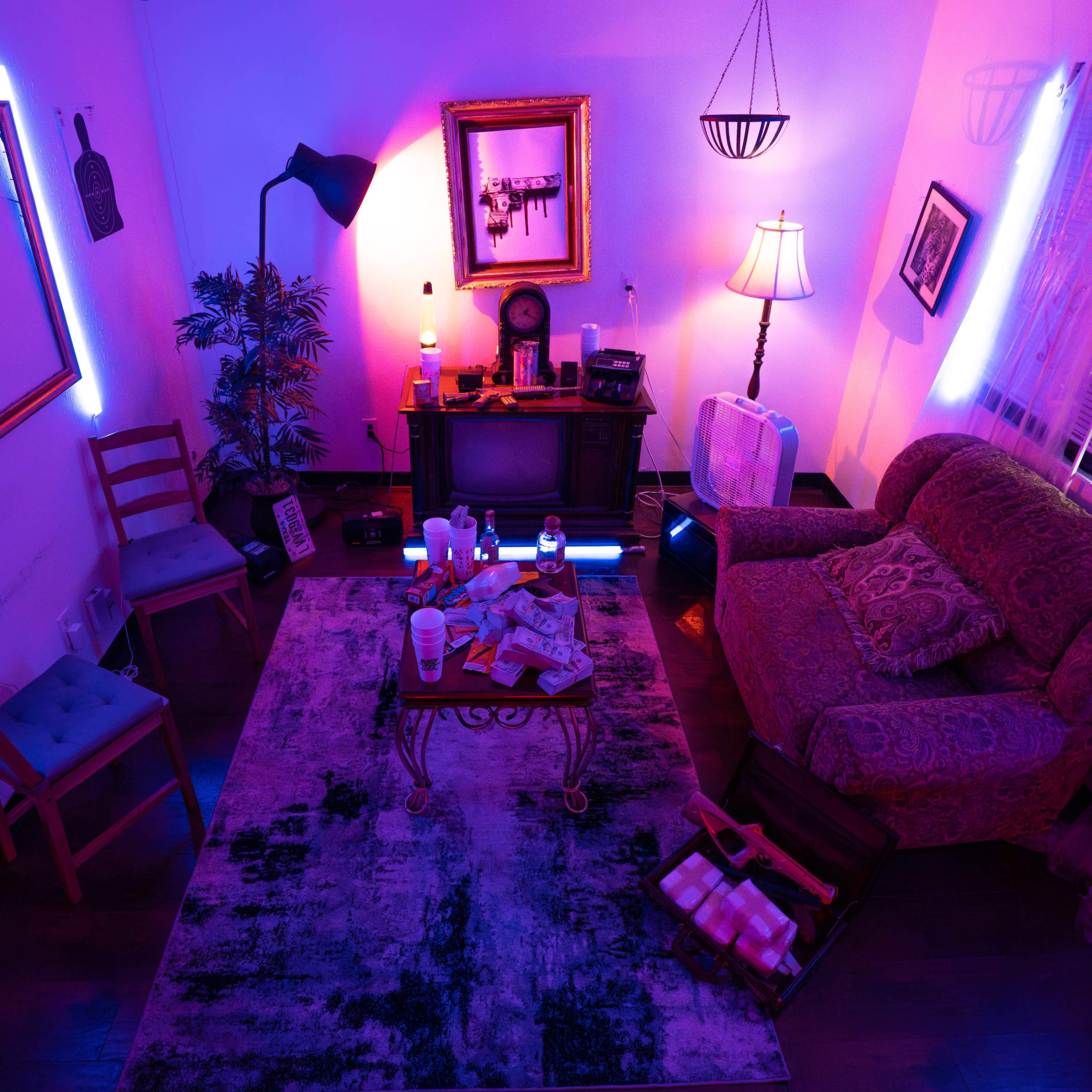 A brightly lit living room featuring a couch, a coffee table with scattered items, a television, and various decorations, all illuminated by purple and blue lighting.