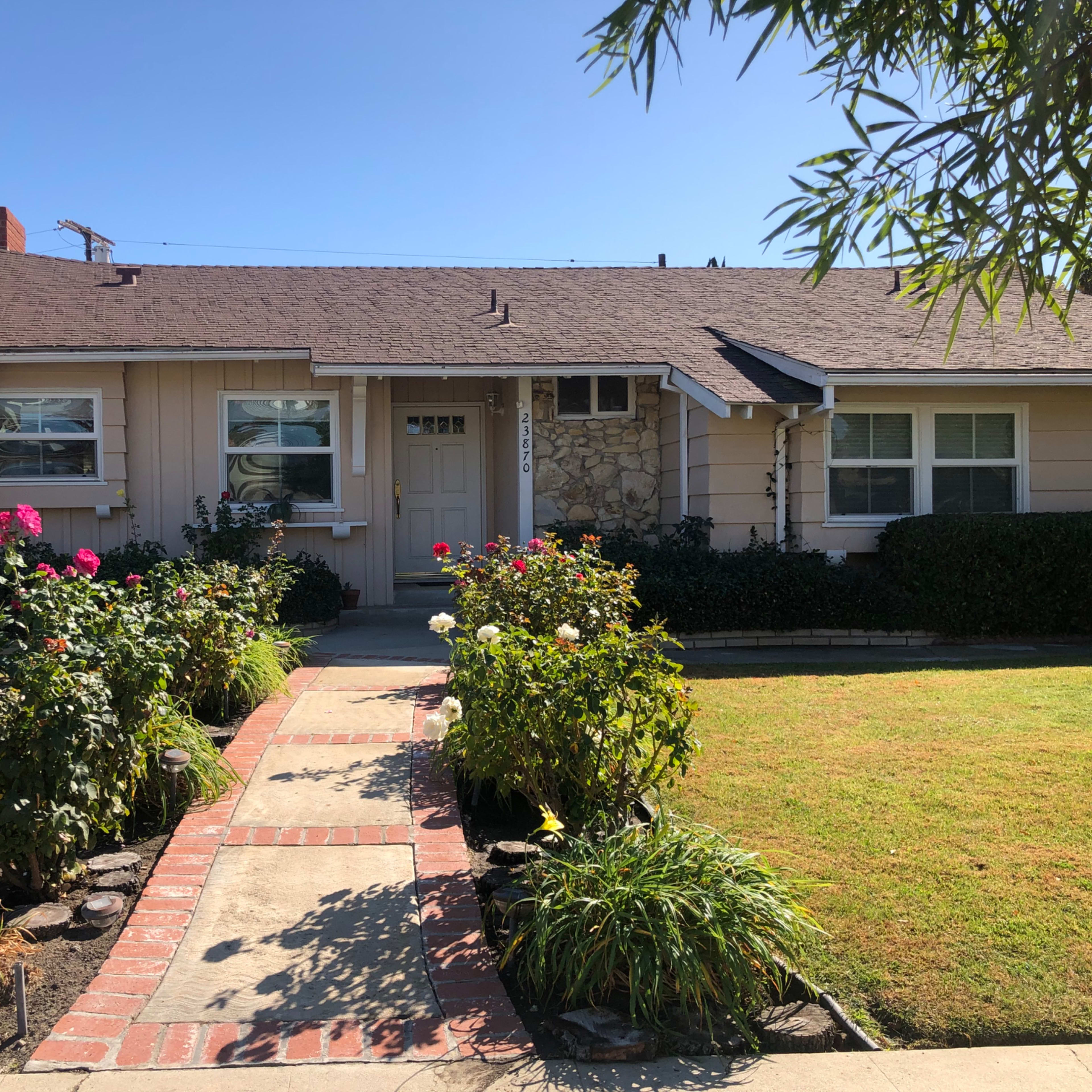 A single-story house with a front walkway bordered by flower beds and a neatly maintained lawn.