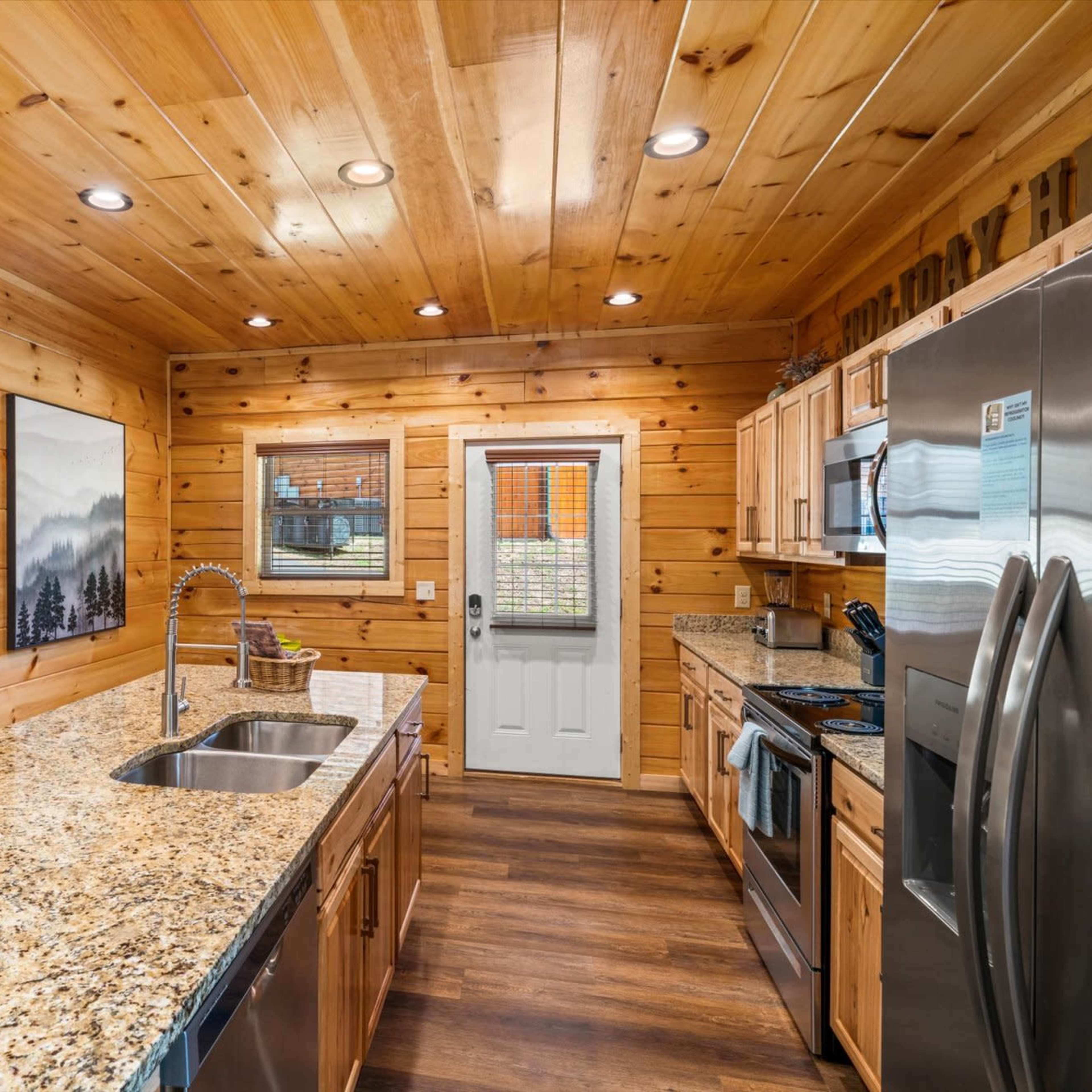 A cozy kitchen with wooden walls, granite countertops, stainless steel appliances, and a view of a door leading outside.