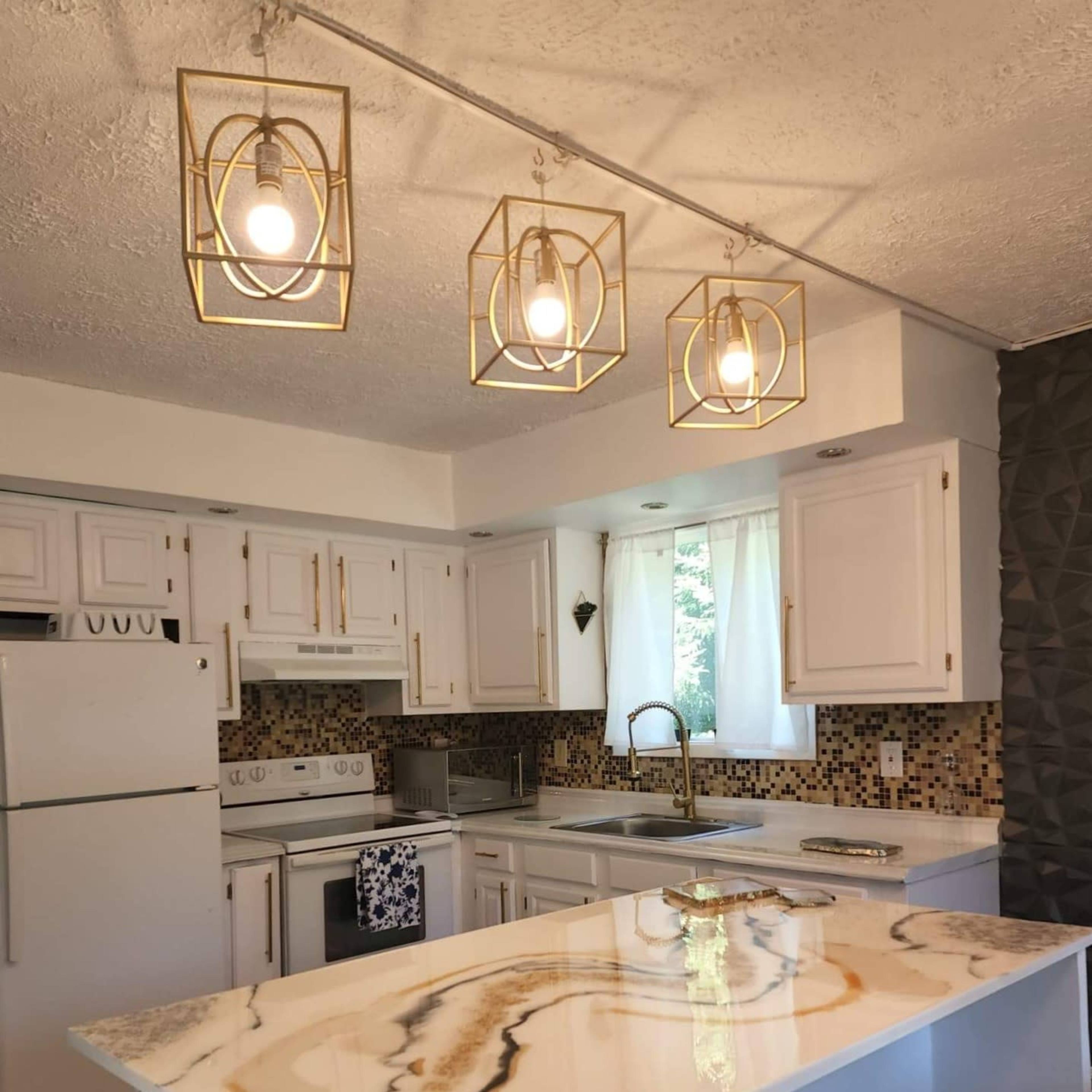 A modern kitchen features white cabinetry, a granite countertop with golden veining, and three hanging light fixtures.