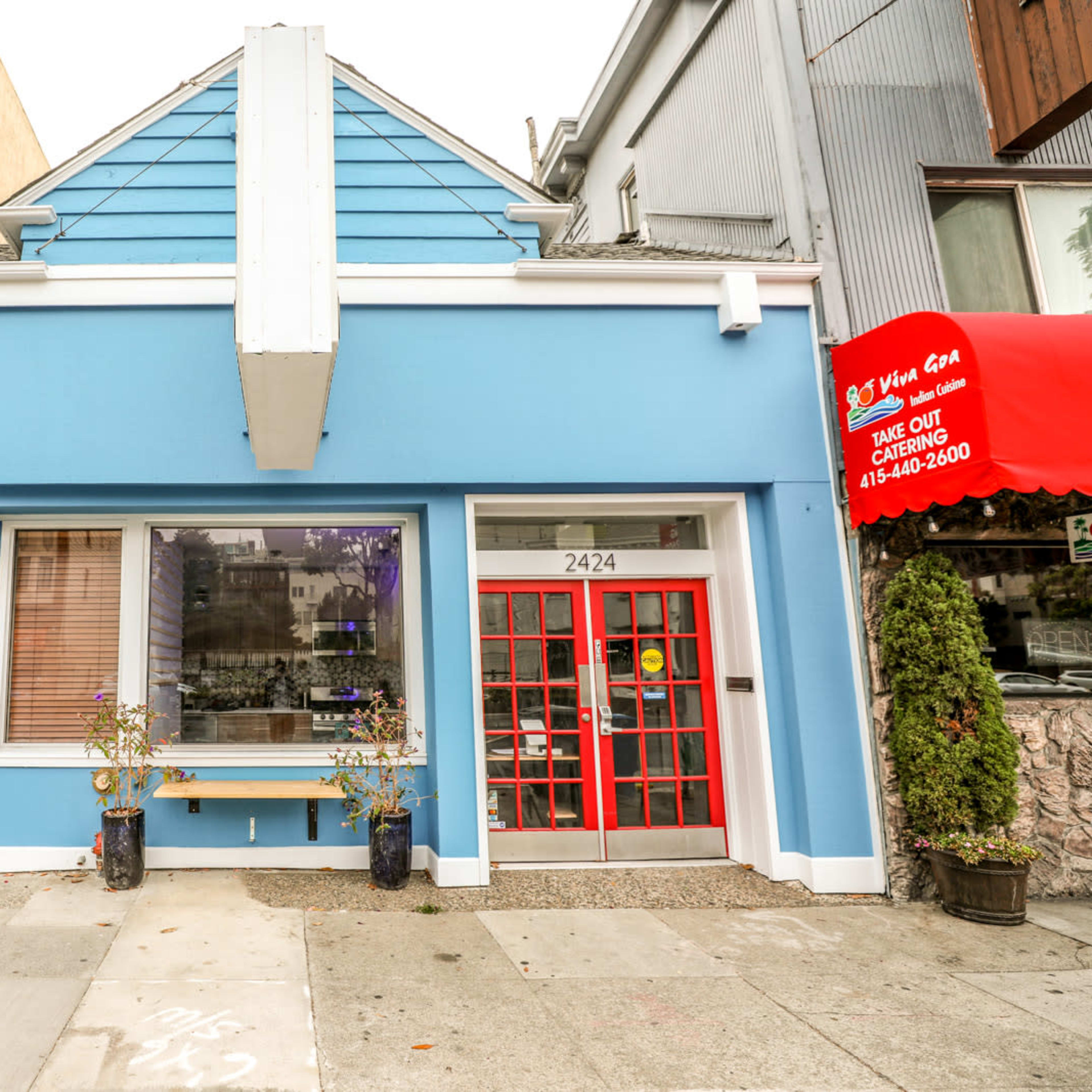A blue building with a red door and a sidewalk lined with a parking meter.
