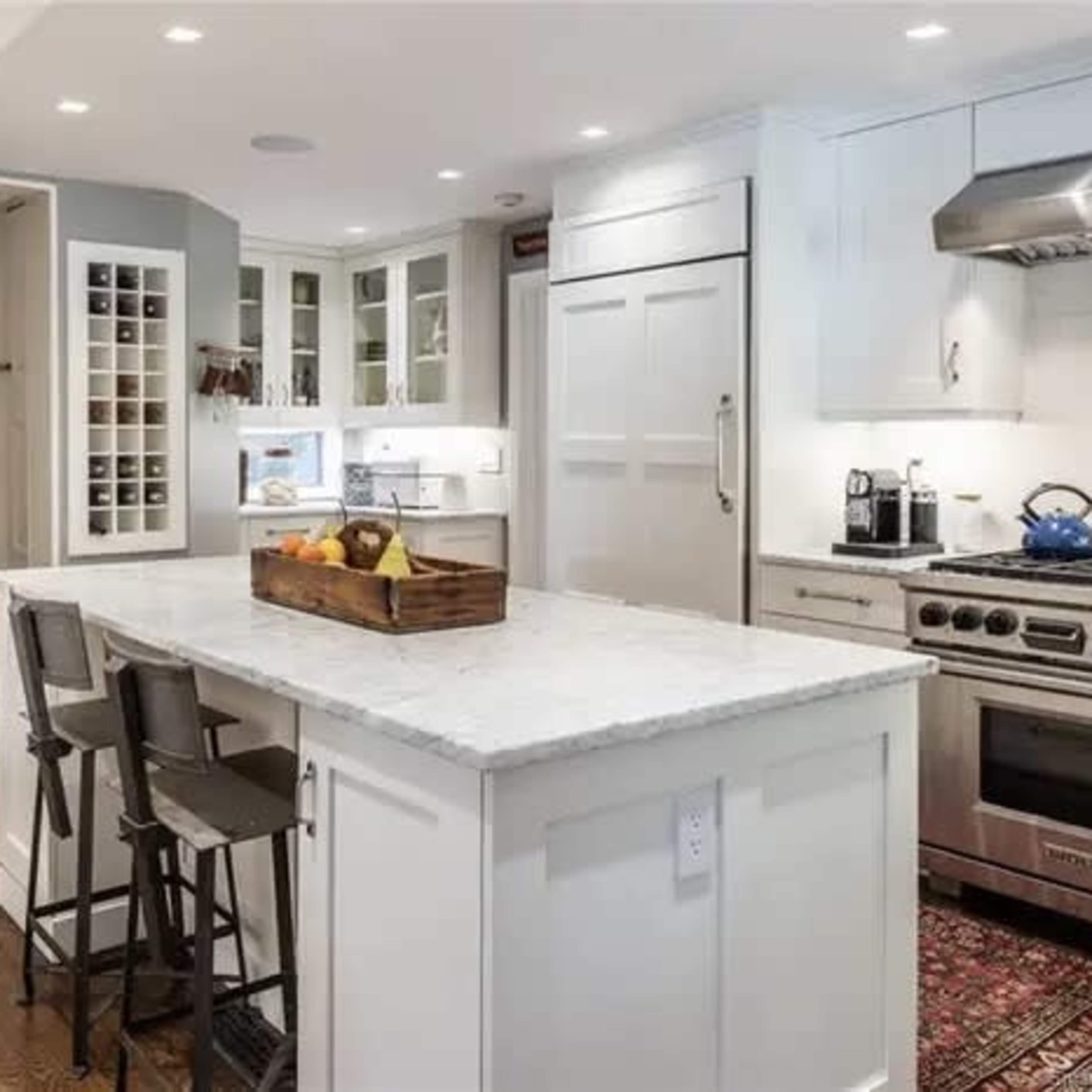 A modern kitchen featuring a central island with a marble countertop, stainless steel appliances, and a staircase leading to an upper level.