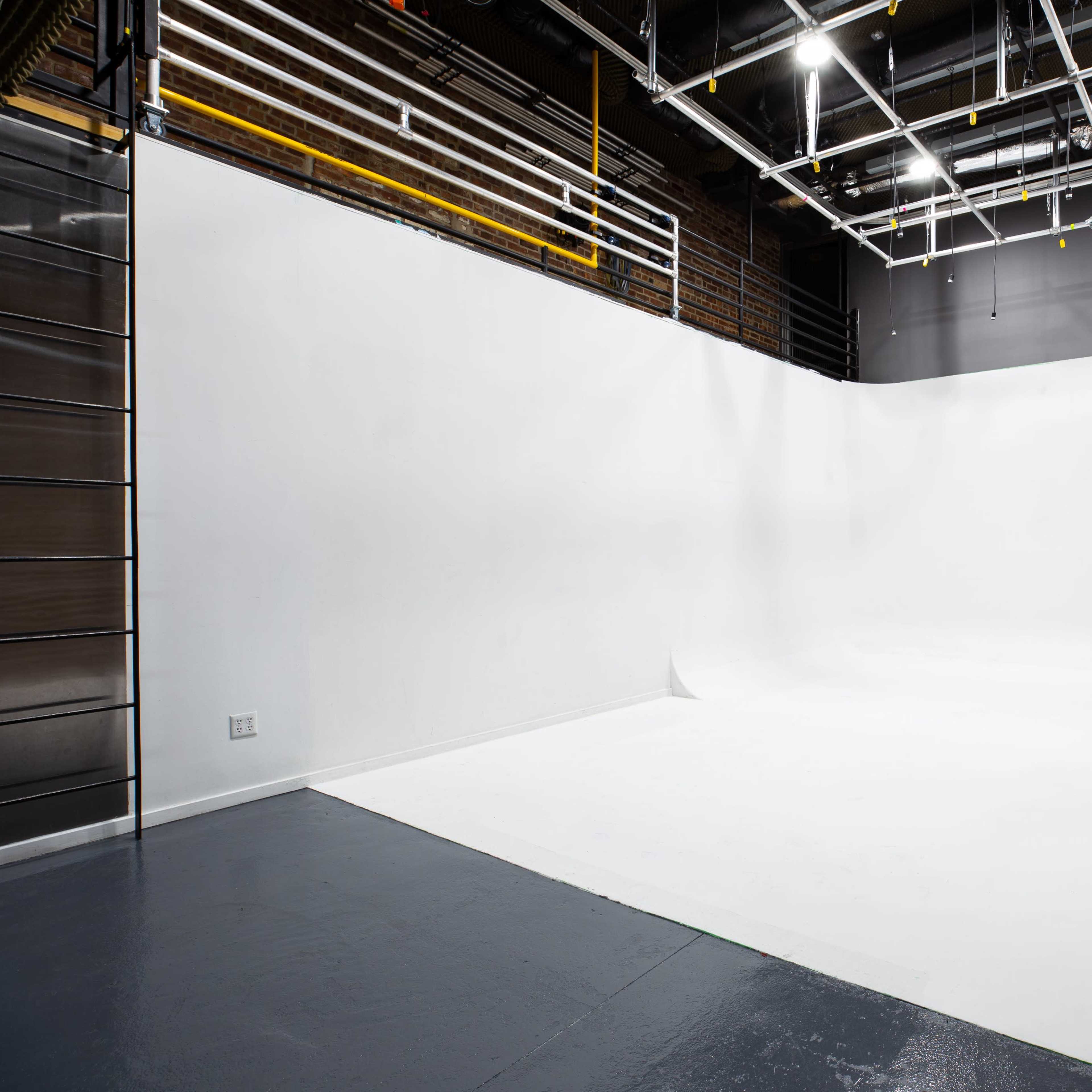 A large, empty photo studio with a seamless white backdrop and exposed brick walls.