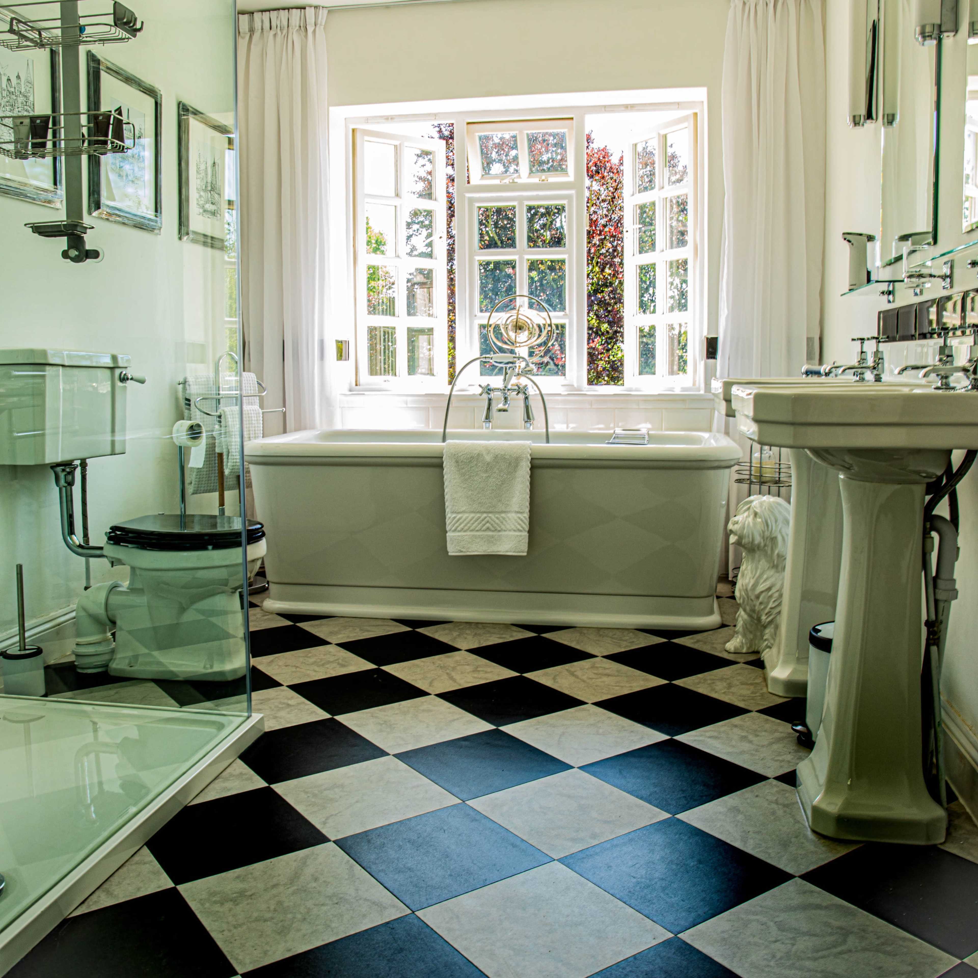 The bathroom features a freestanding bathtub, a glass-enclosed shower, and a window with multiple panes allowing natural light to fill the space.