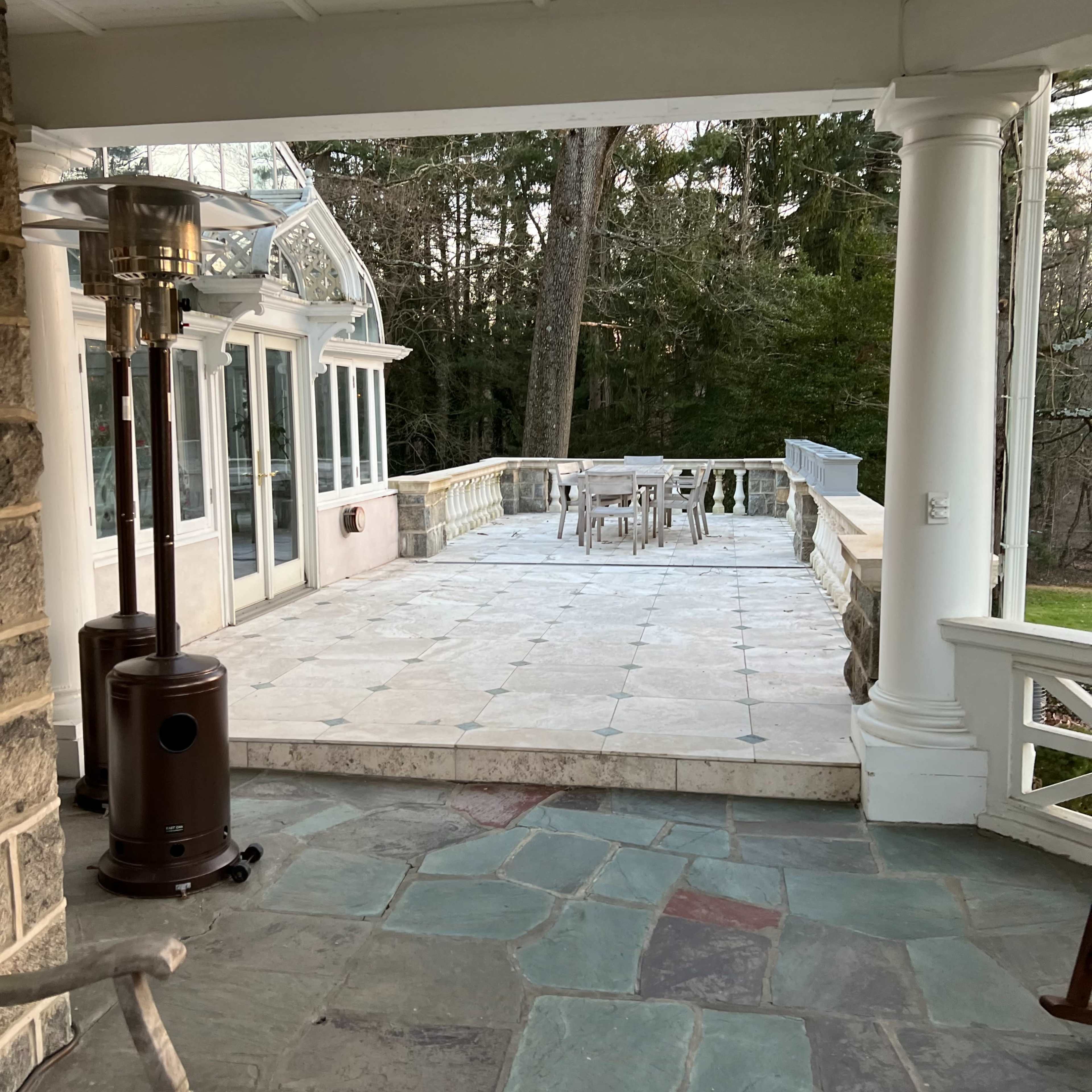 A stone patio with a view of a wooded area, featuring a table and chairs set up for outdoor dining.