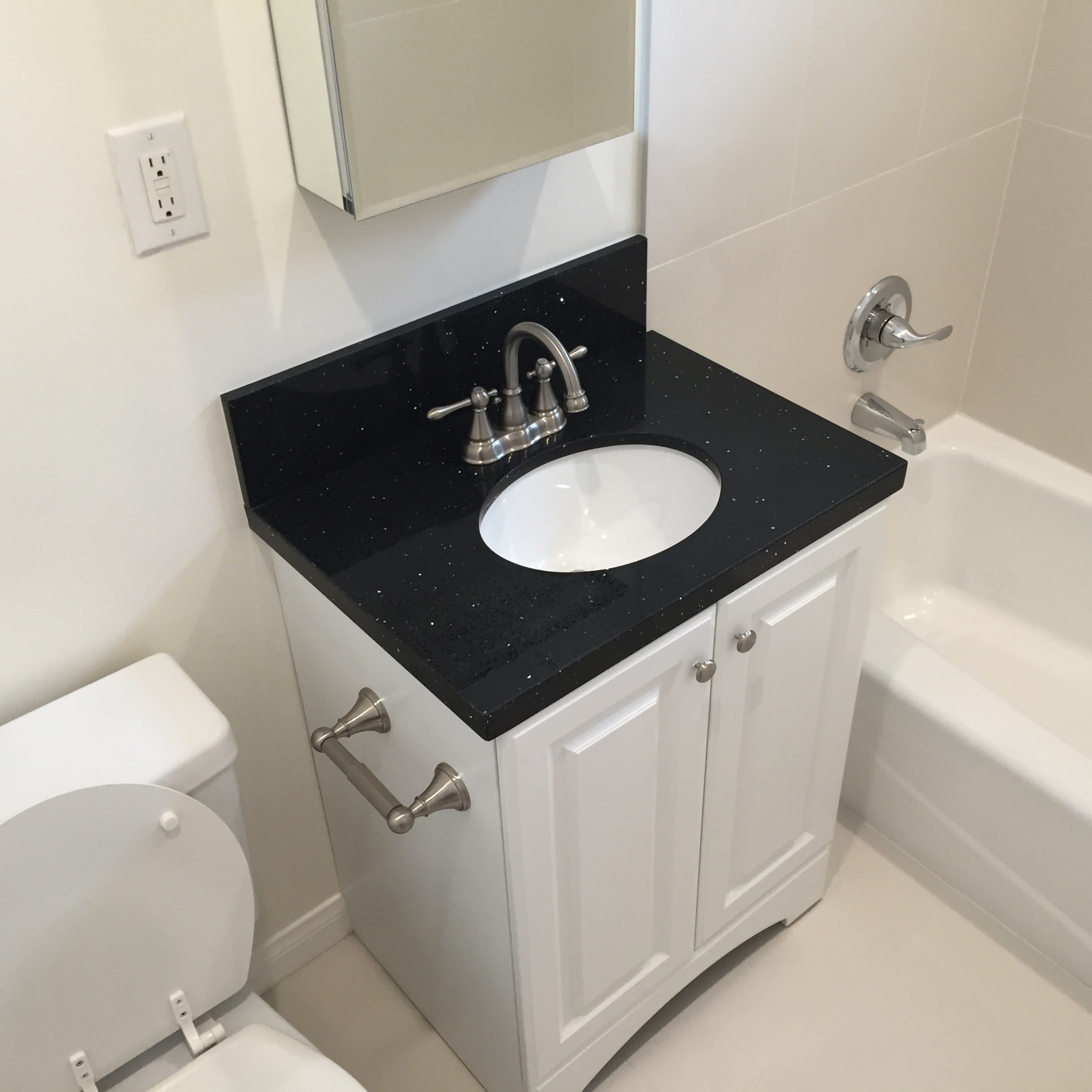 A bathroom featuring a white vanity with a black countertop, a sink, a mirror, a toilet, and a bathtub with a shower.