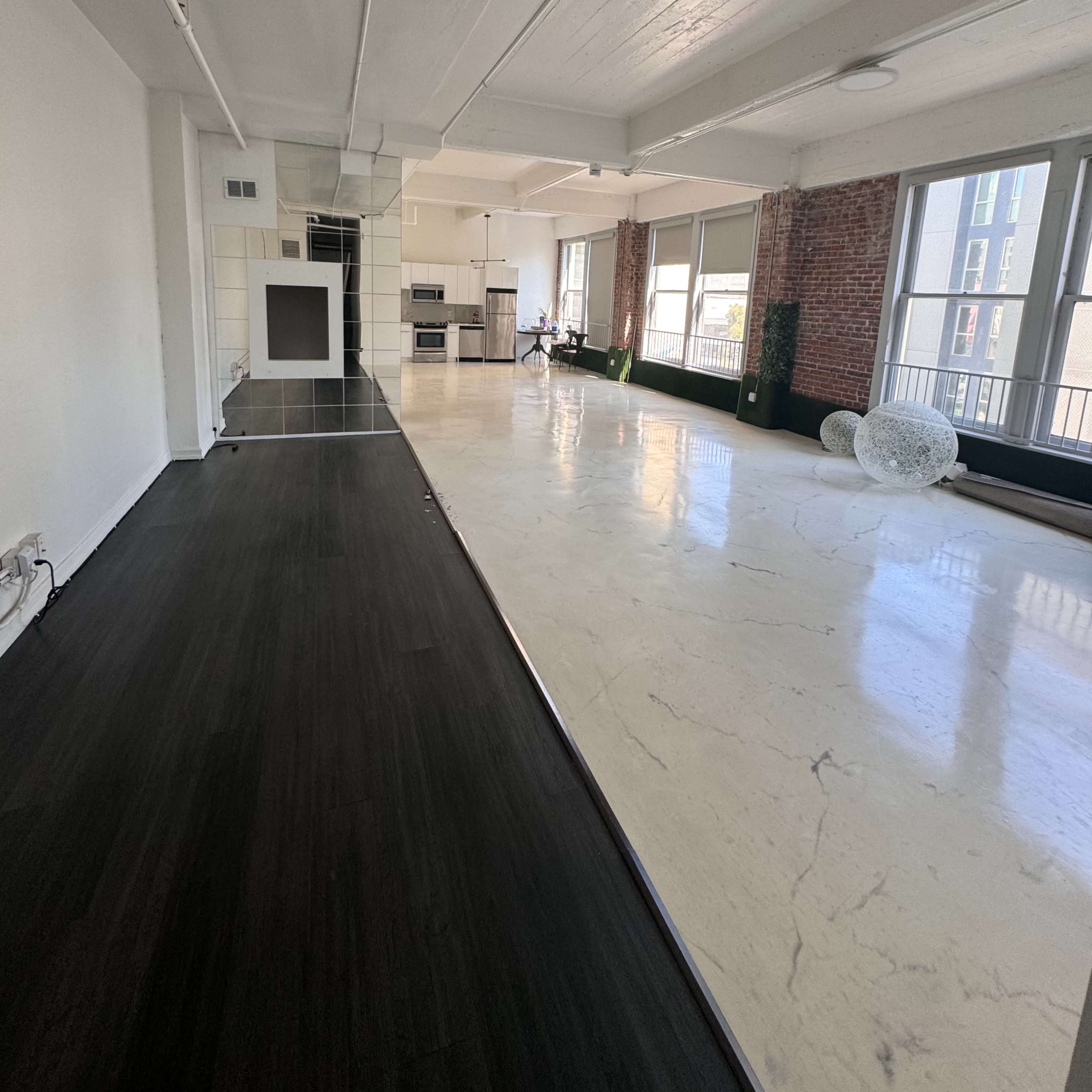 A spacious, modern apartment with a combination of dark and light flooring, large windows, and exposed brick walls.