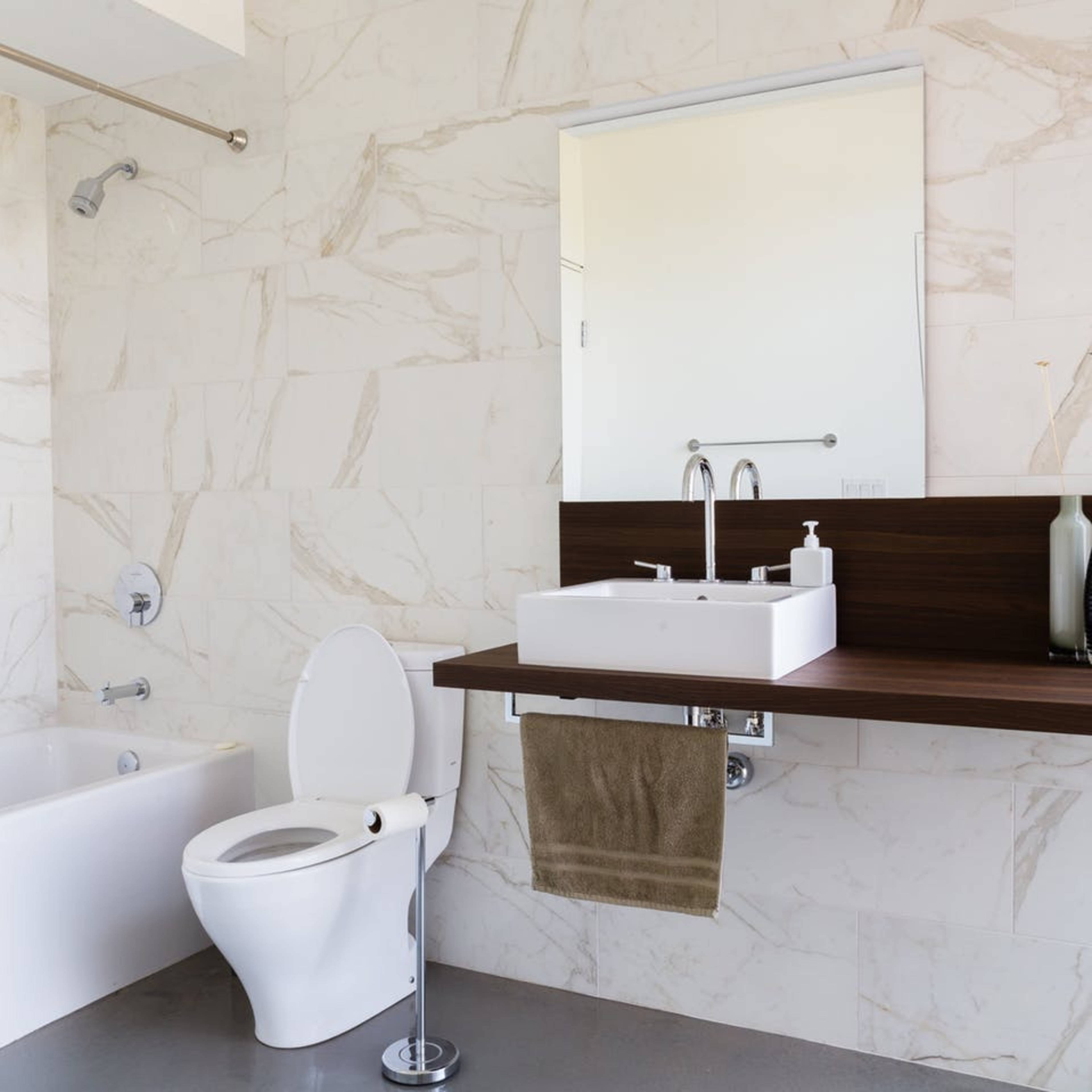 A modern bathroom with a bathtub, toilet, and a wall-mounted sink with a rectangular mirror above it.