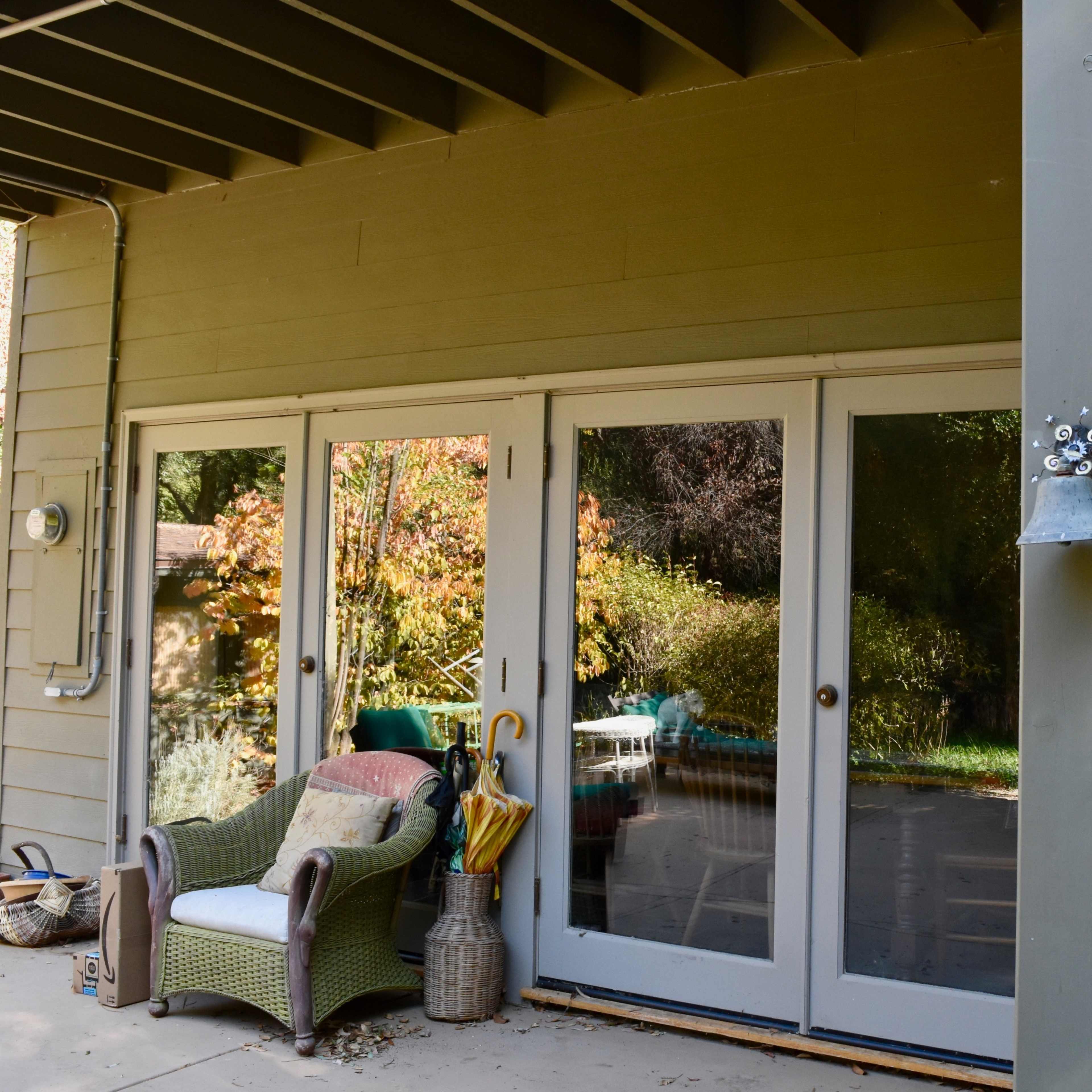 A patio area with multiple glass doors reflecting a garden and outdoor seating.