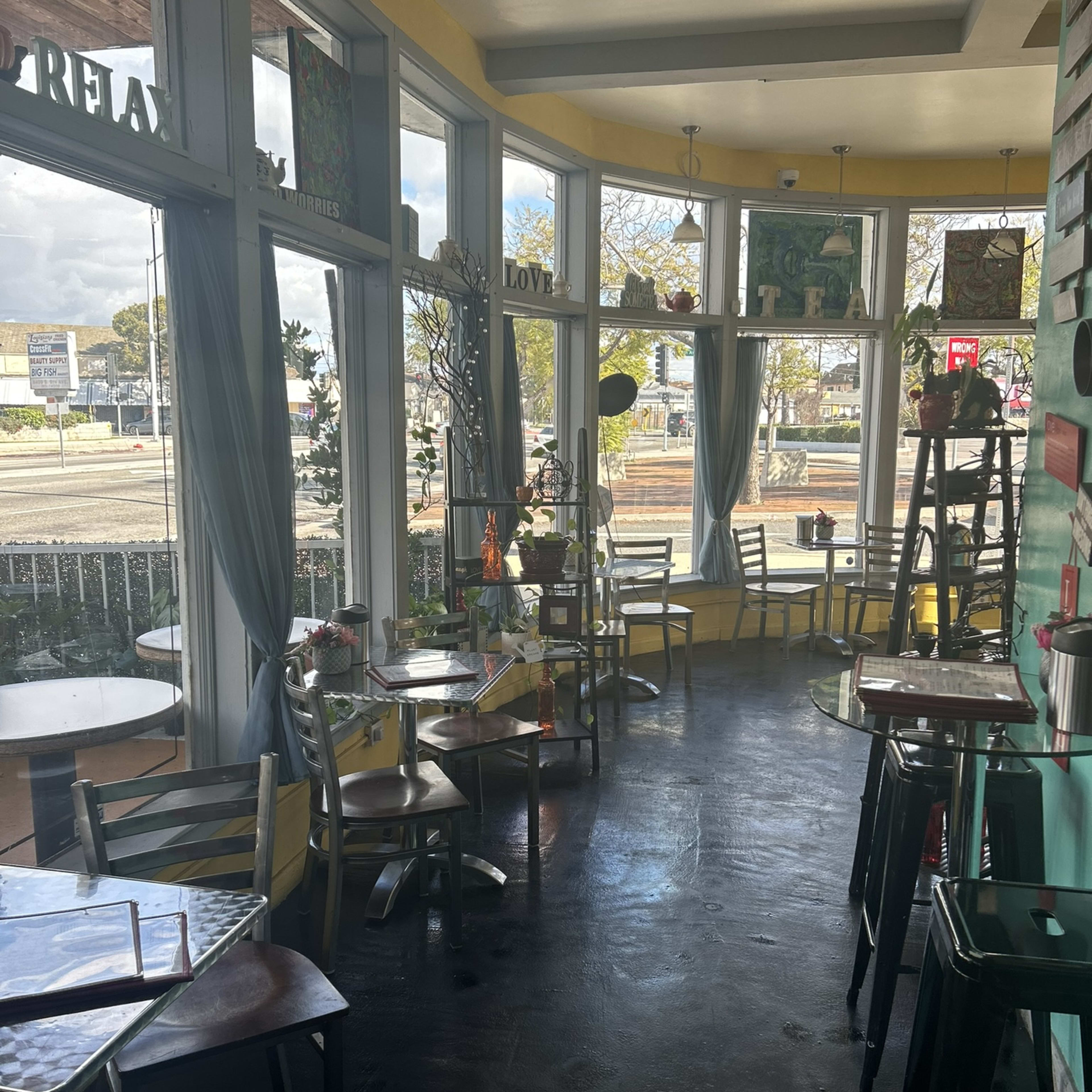 A brightly lit café interior with several tables and chairs arranged near large windows.