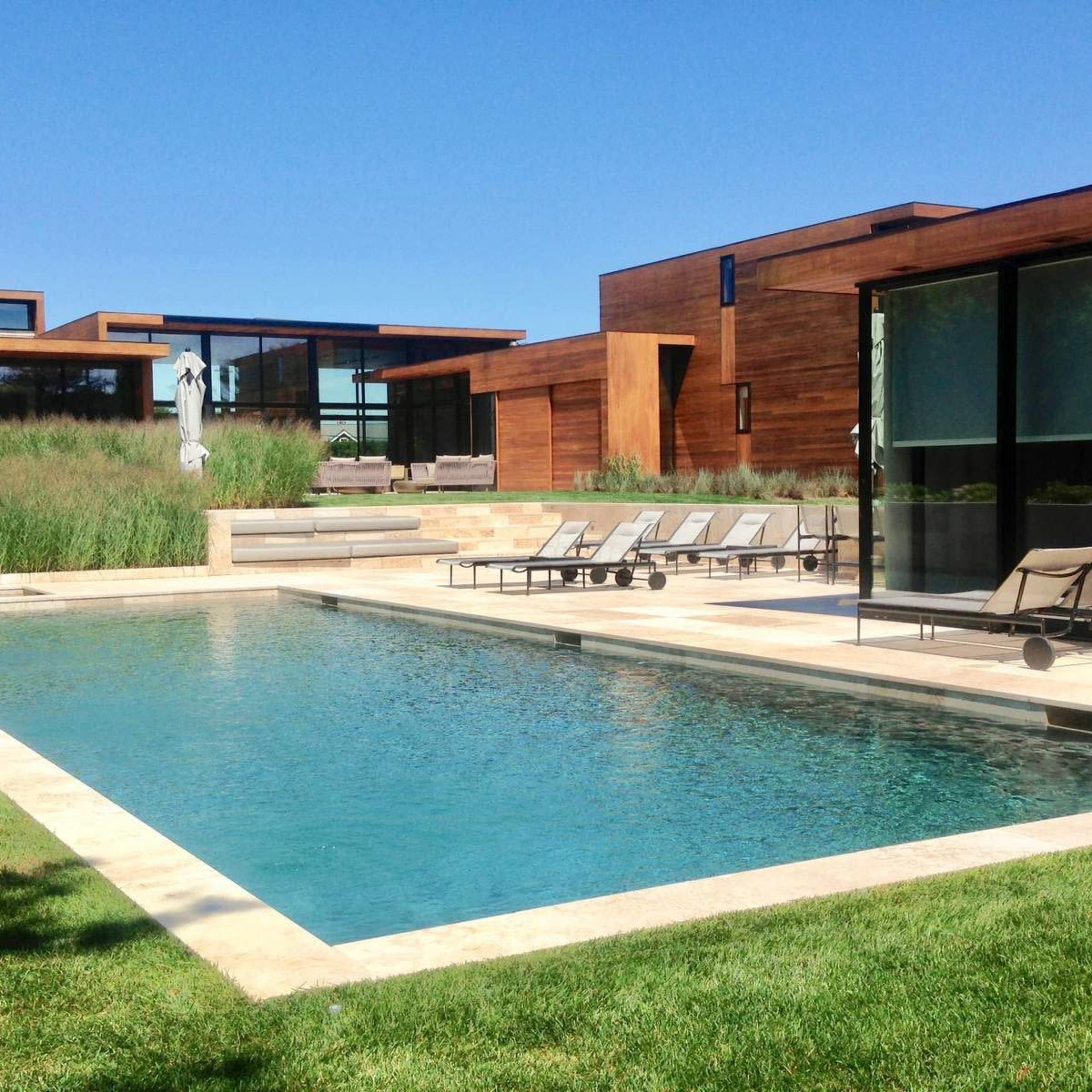 A modern house with wooden exterior walls, a swimming pool, and lounge chairs, surrounded by well-maintained grass and landscaping.