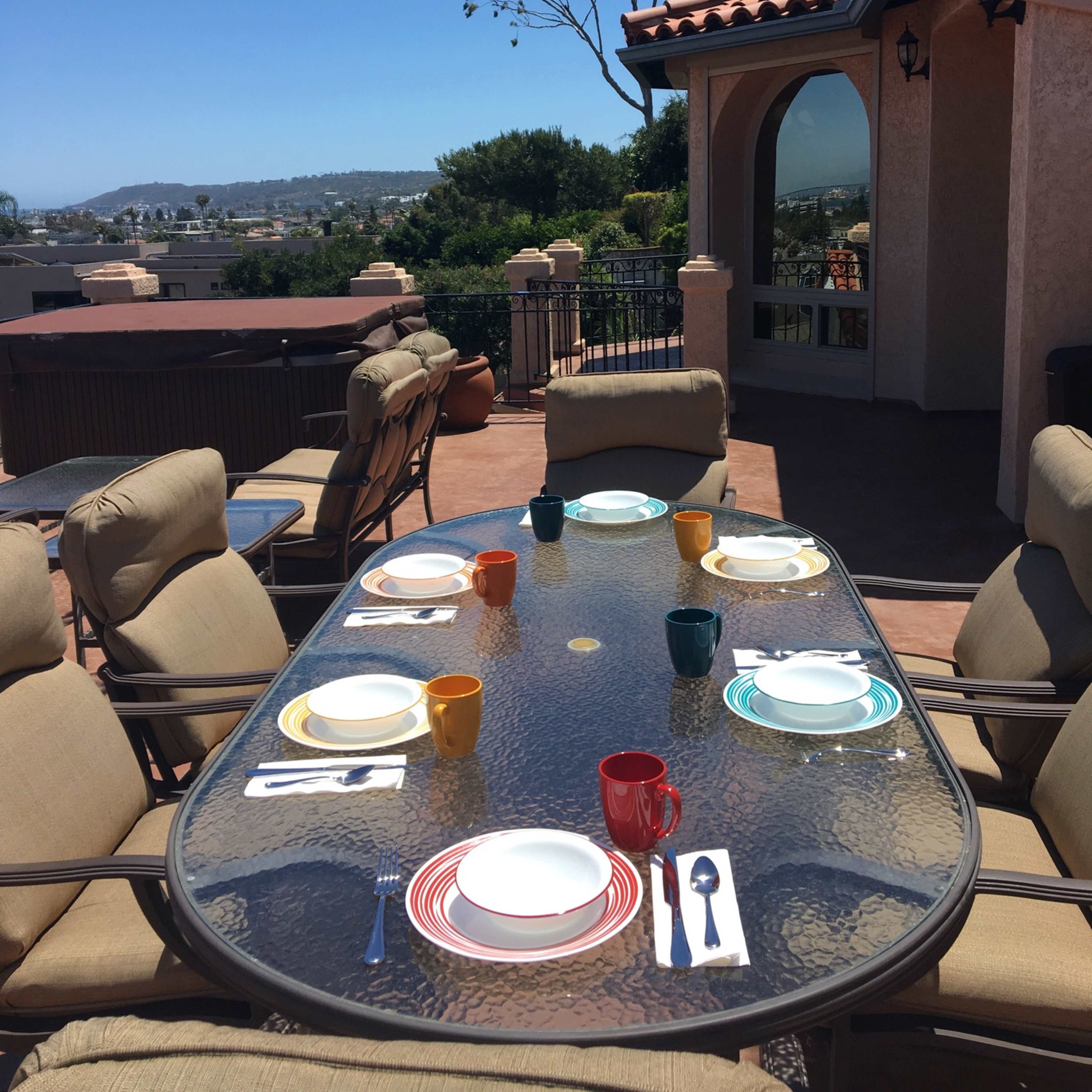 A table set with colorful dishes and utensils is positioned on a patio overlooking a scenic view.