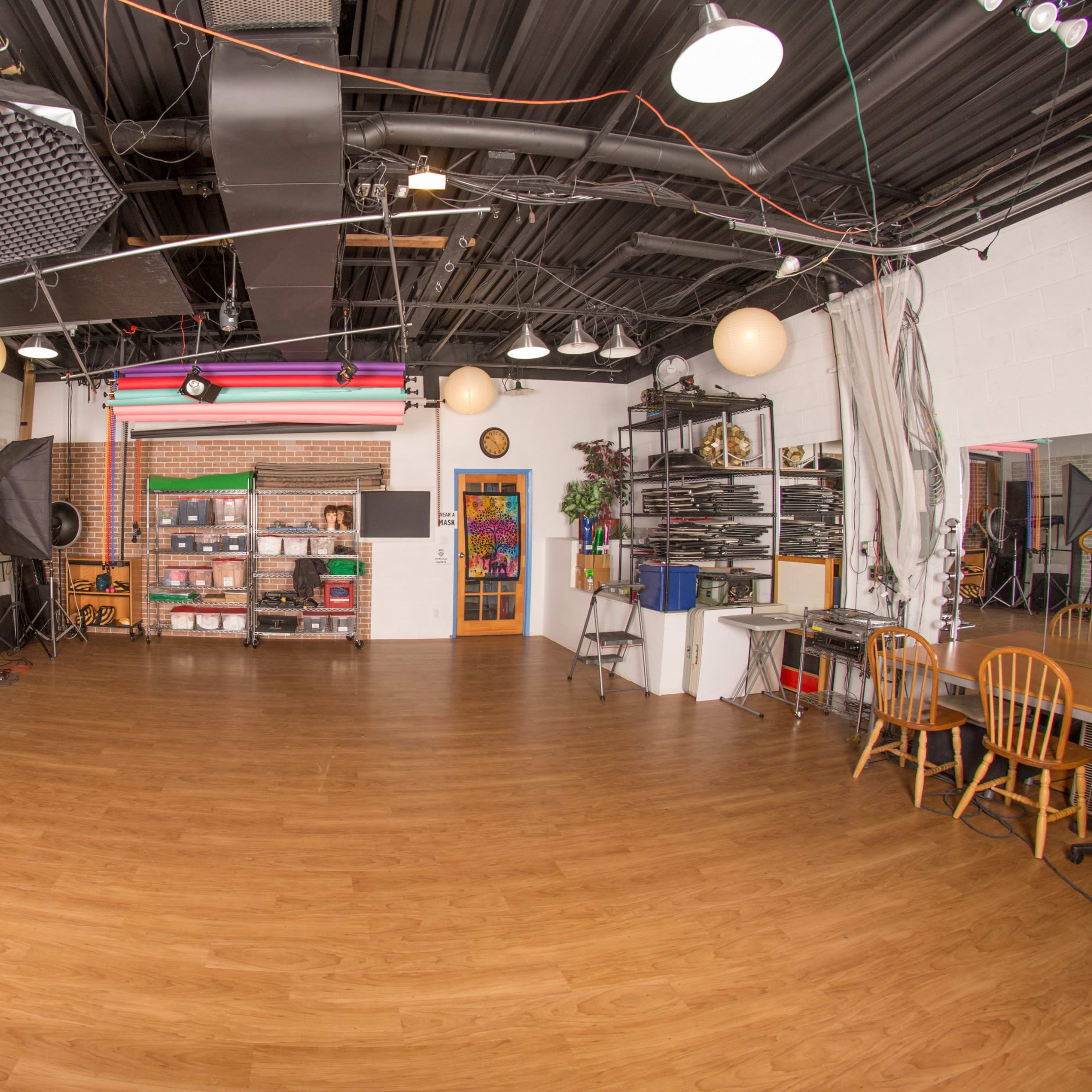 A spacious photography studio features various lighting equipment, props, and a wooden floor.