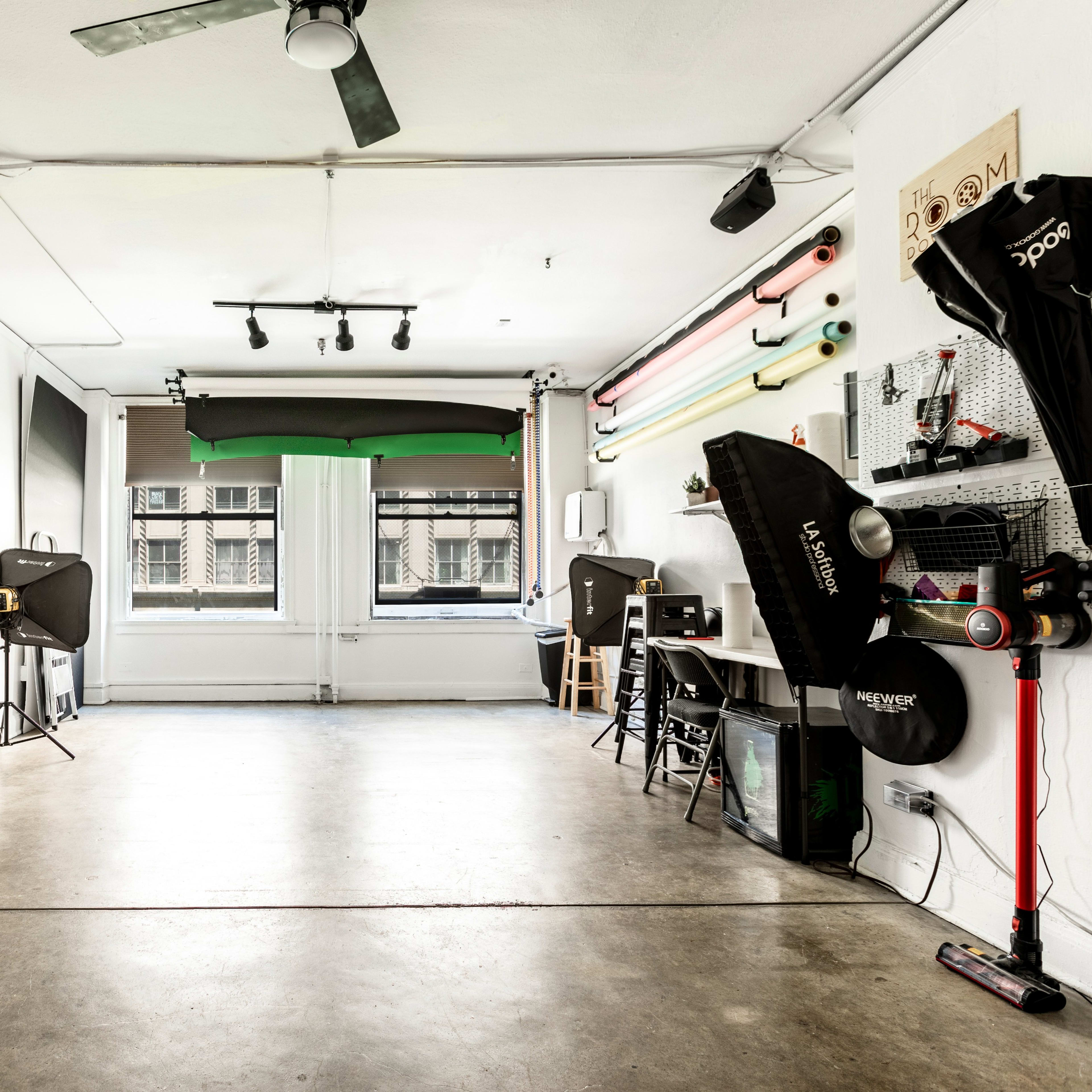 A spacious photography studio with a concrete floor, equipped with various lighting equipment and backdrops along the walls.