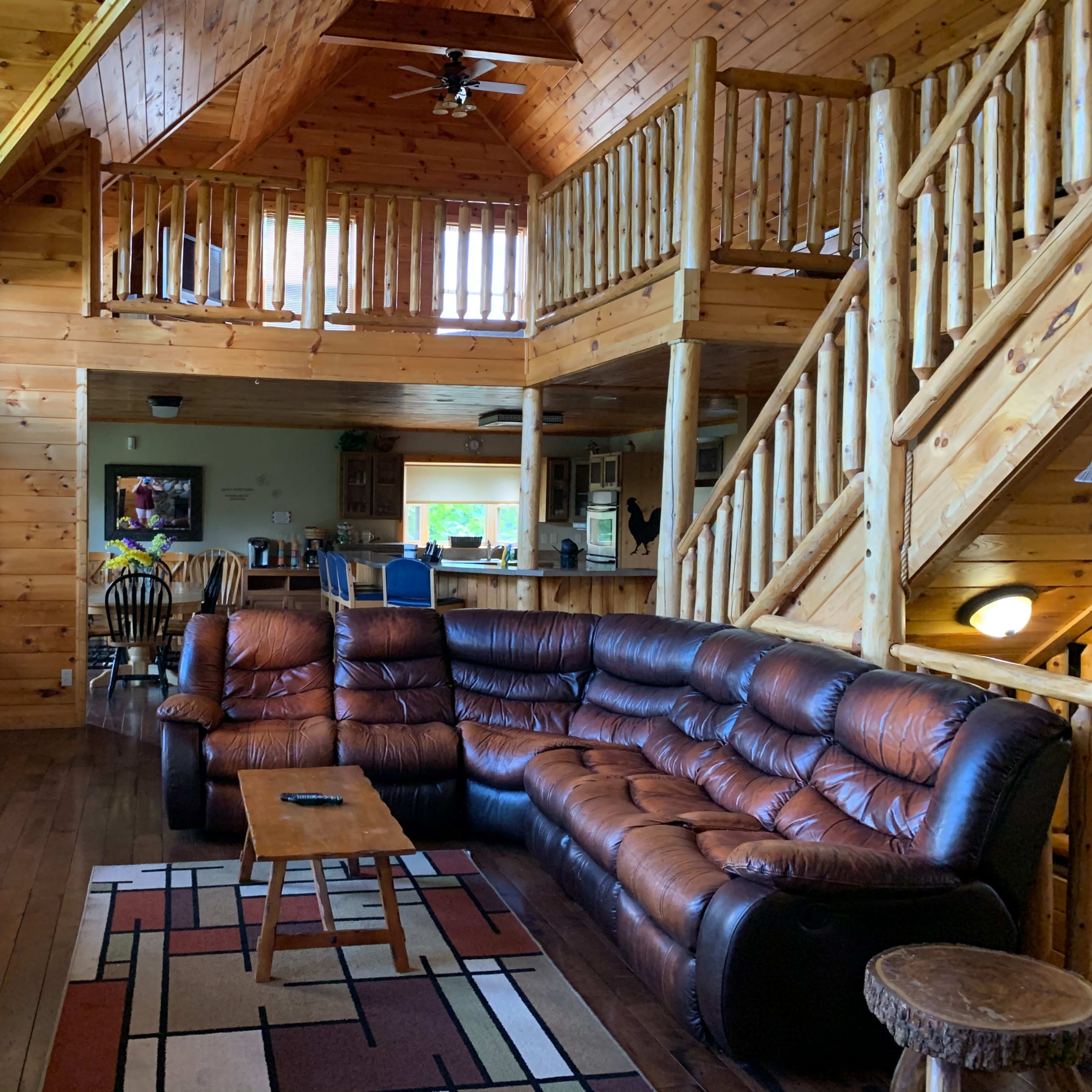 A large wooden cabin interior with a couch, coffee table, and two levels featuring a staircase and a kitchen area.
