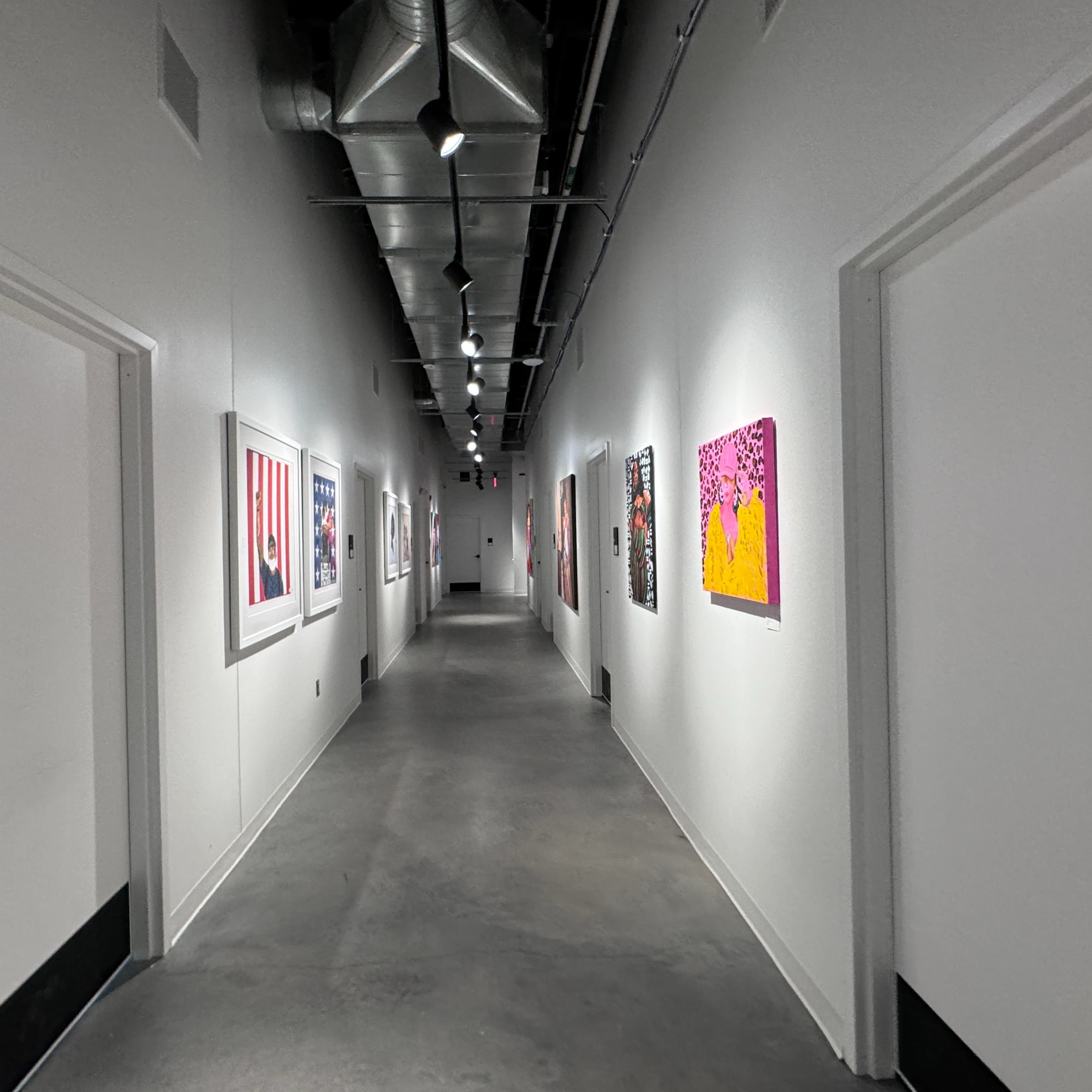 A long hallway with white walls features various colorful artworks hanging on either side.