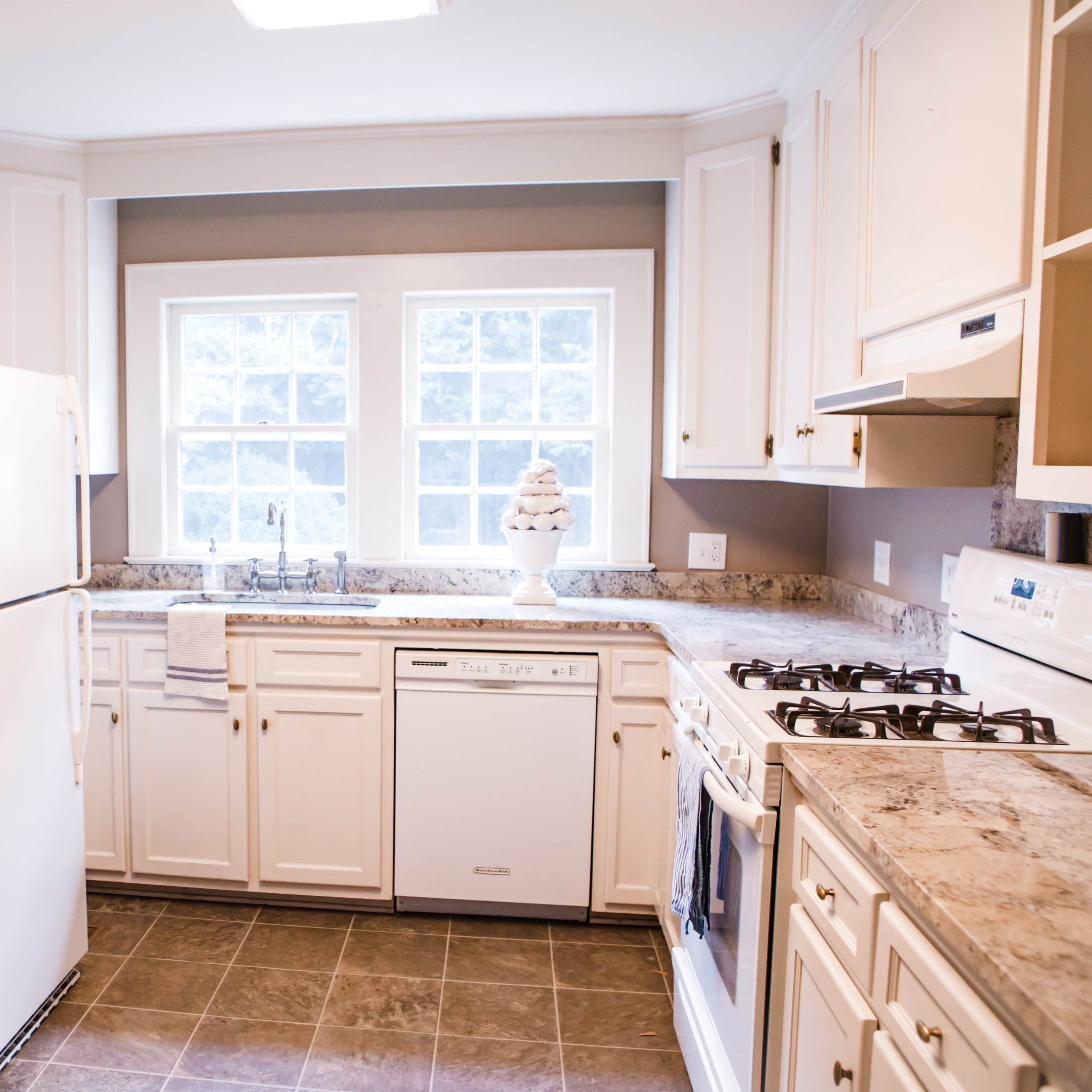 A modern kitchen with white cabinets, a beige countertop, and a window above the sink.