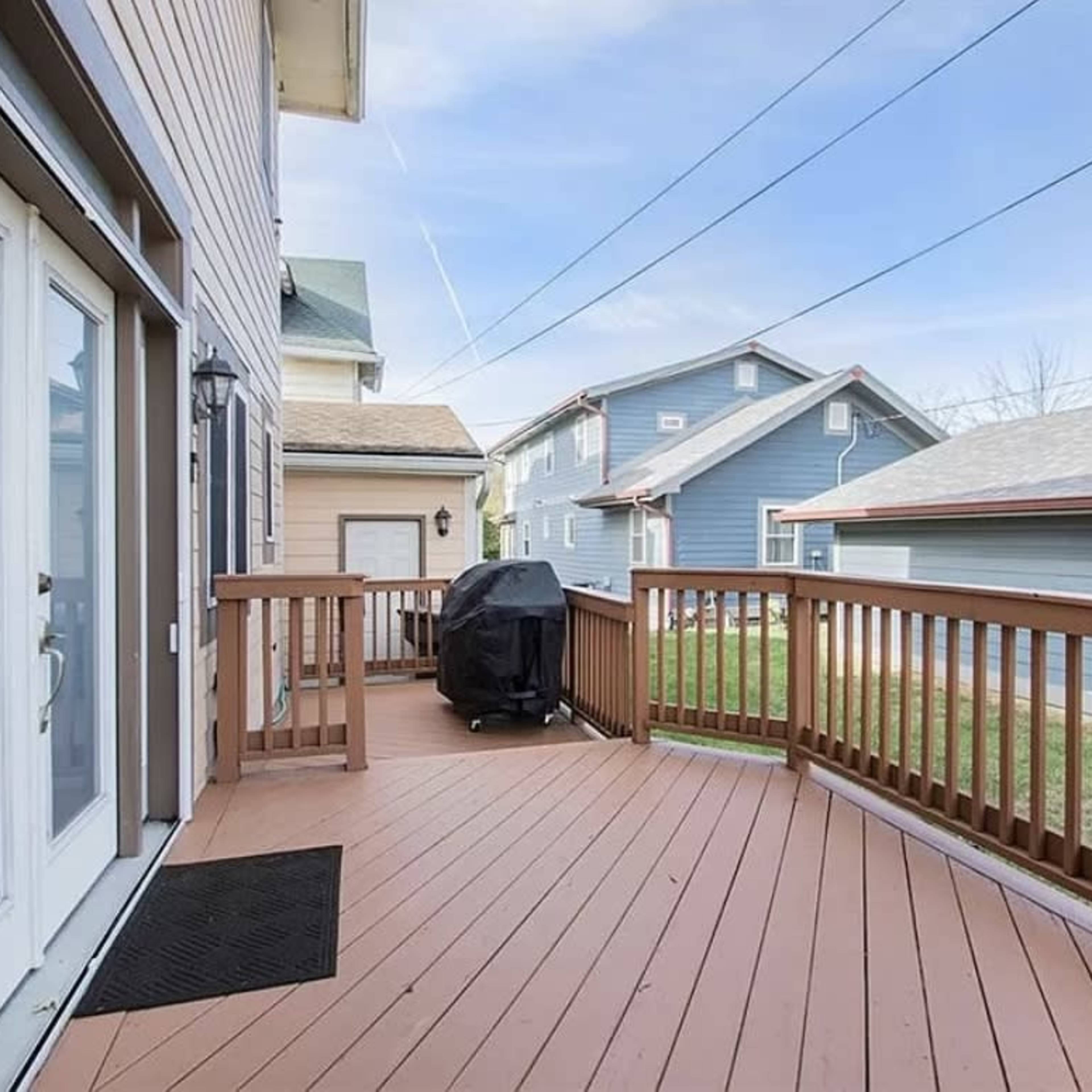 A wooden deck with a black grill, surrounded by houses and a clear blue sky.