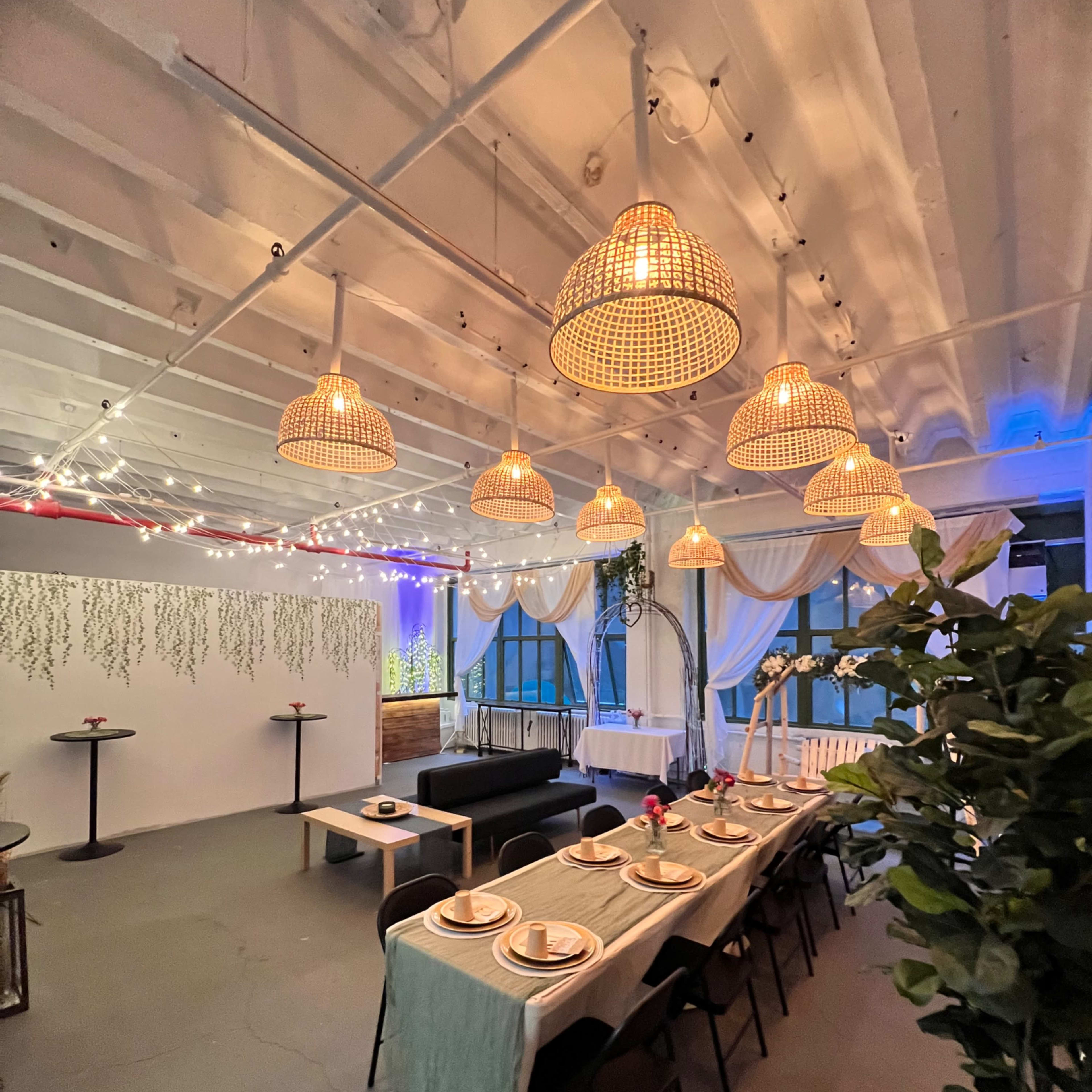 A well-lit dining area with a long table set for a meal, surrounded by decorative hanging lamps and plants.