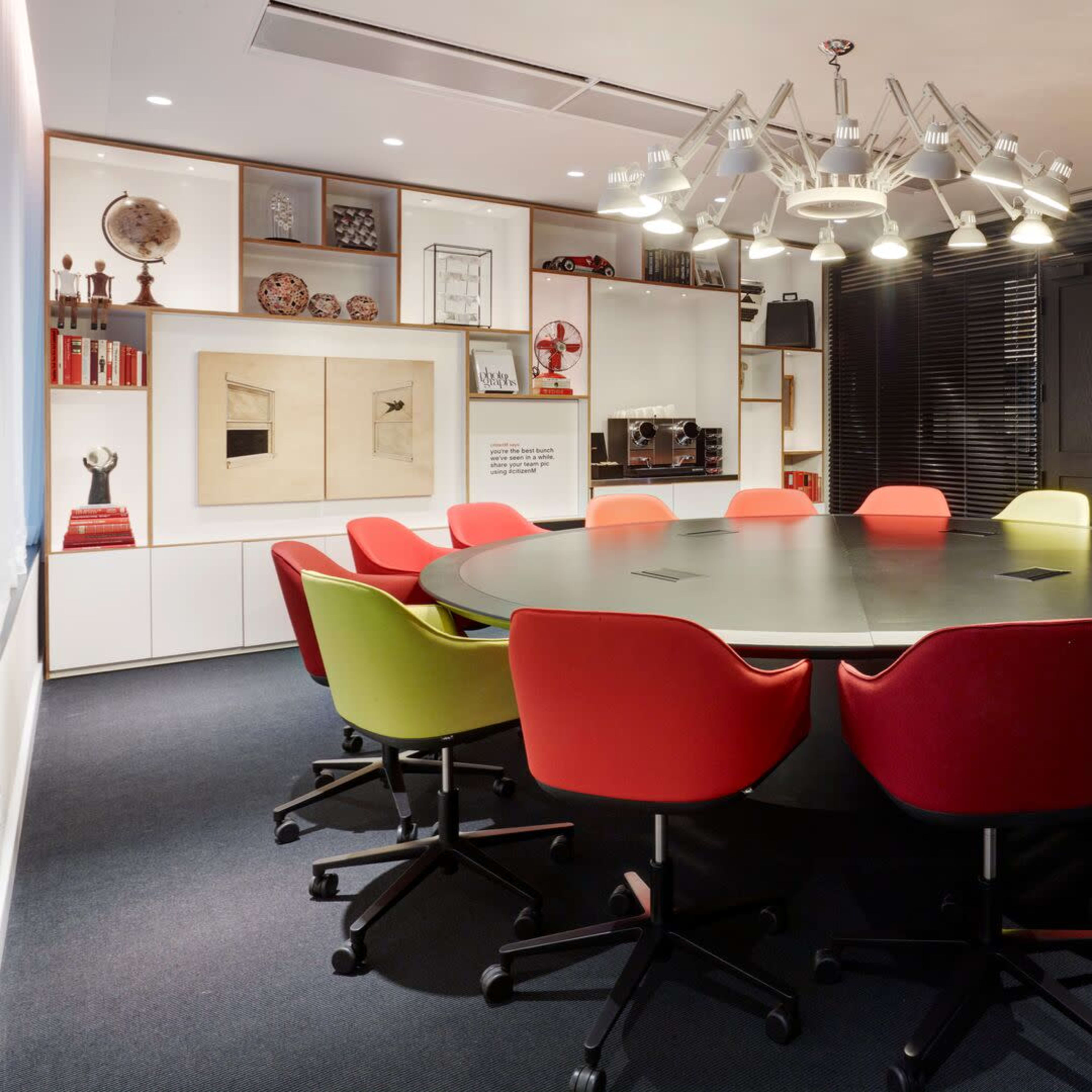 A circular conference table surrounded by colorful chairs is set in a modern meeting room with large windows and artistic decor.