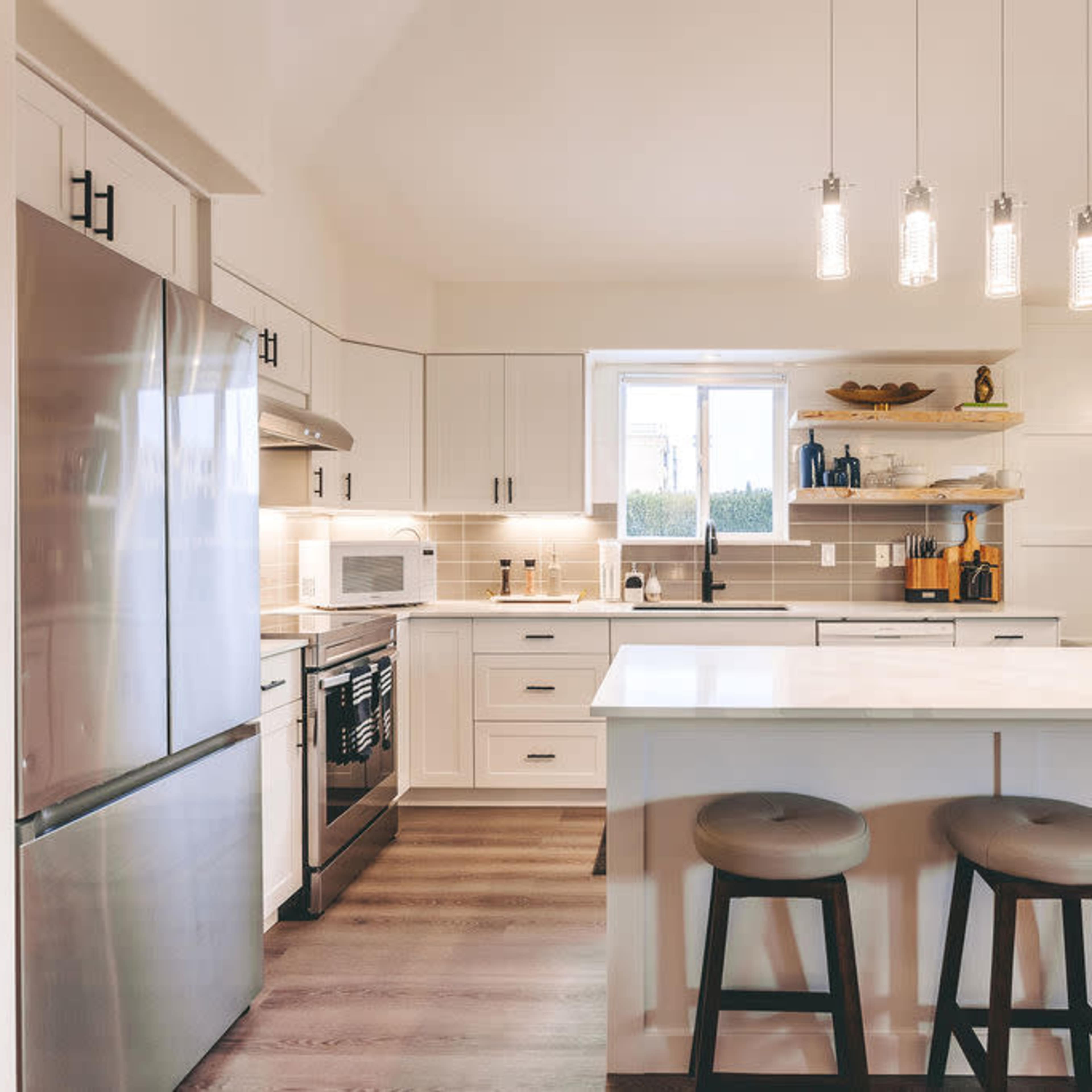 A modern kitchen with white cabinetry, a large island, and pendant lighting above the bar stools.