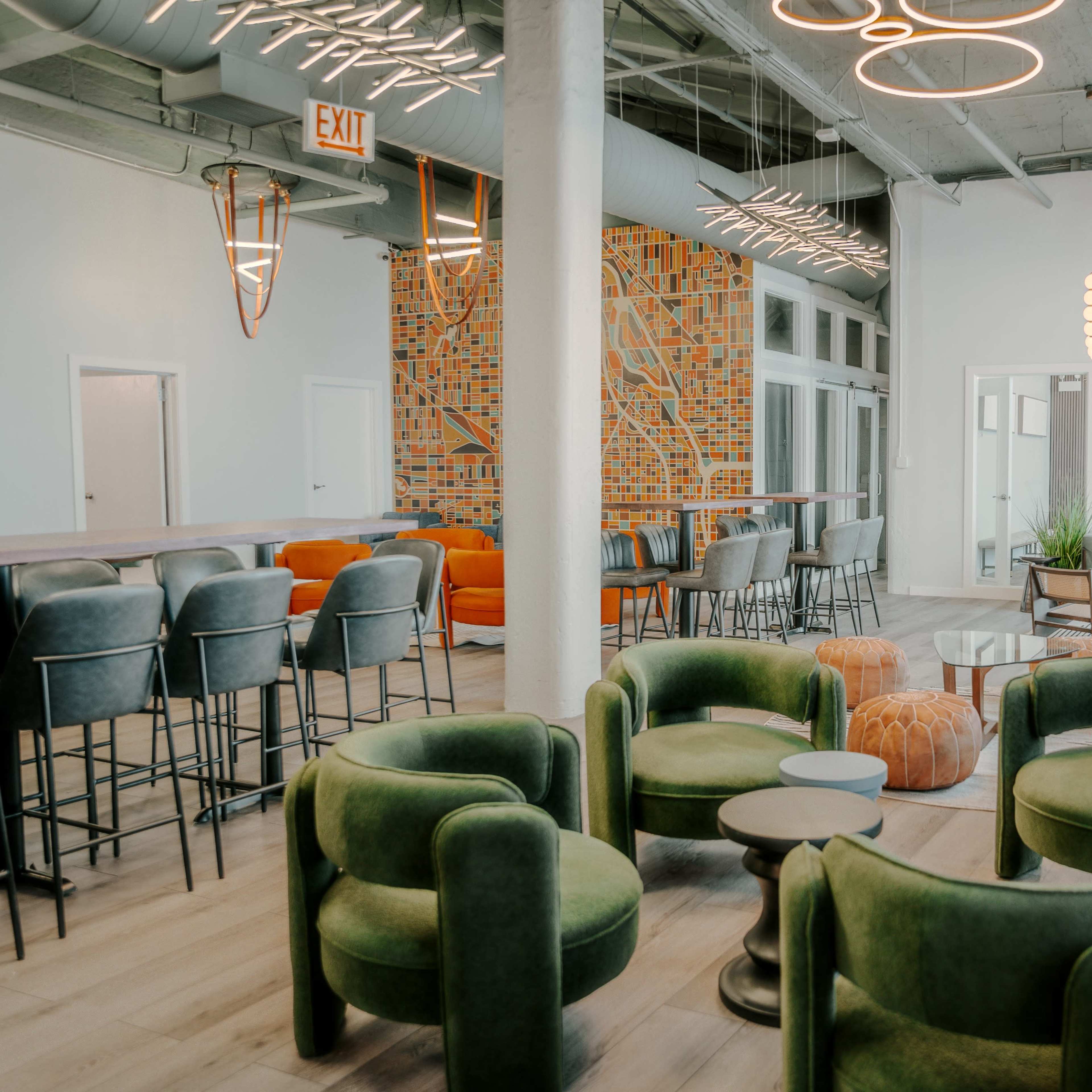 A modern lounge area featuring green armchairs, a mix of seating options, a patterned accent wall, and large windows.