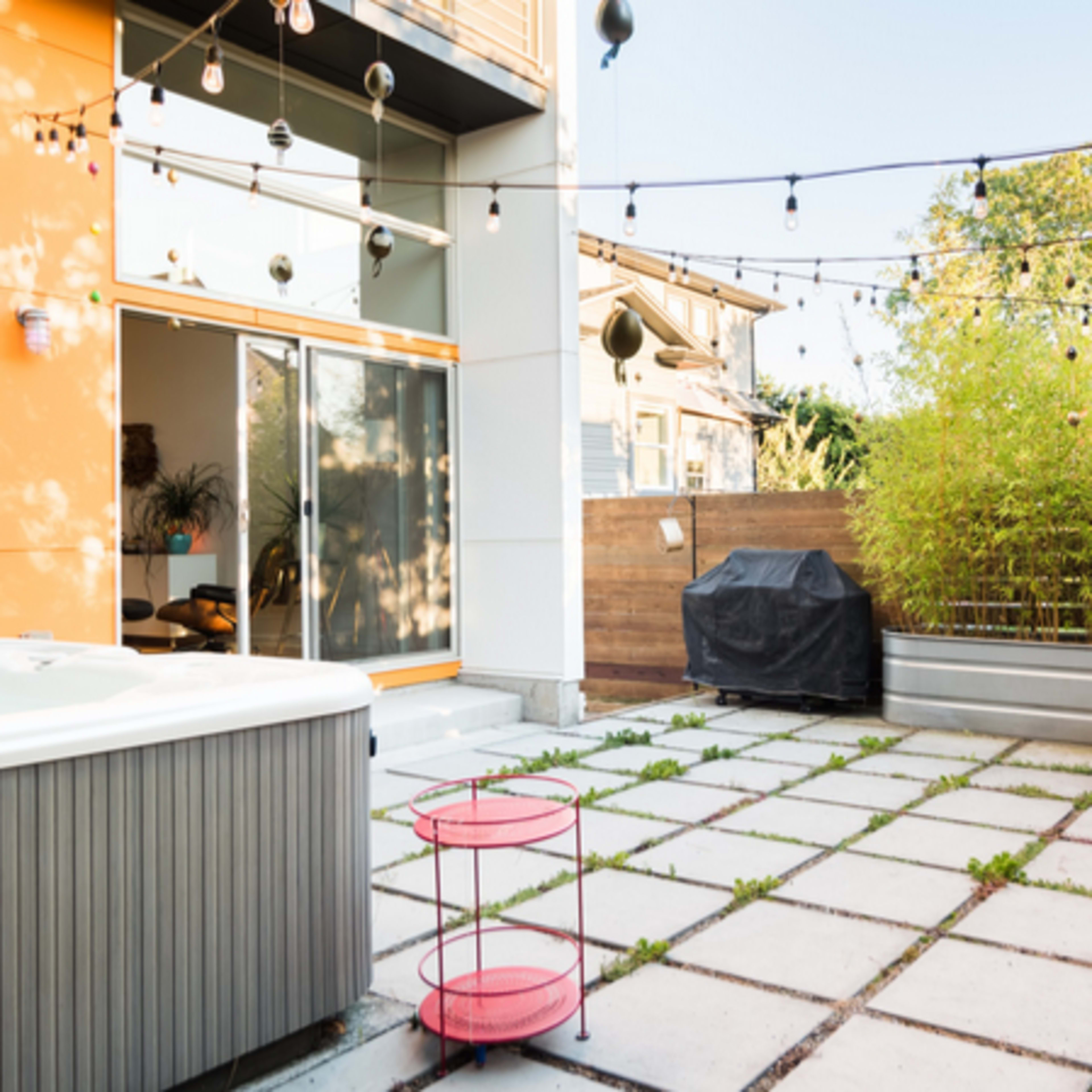 A modern outdoor patio with a hot tub, string lights overhead, and potted plants creating a cozy atmosphere.