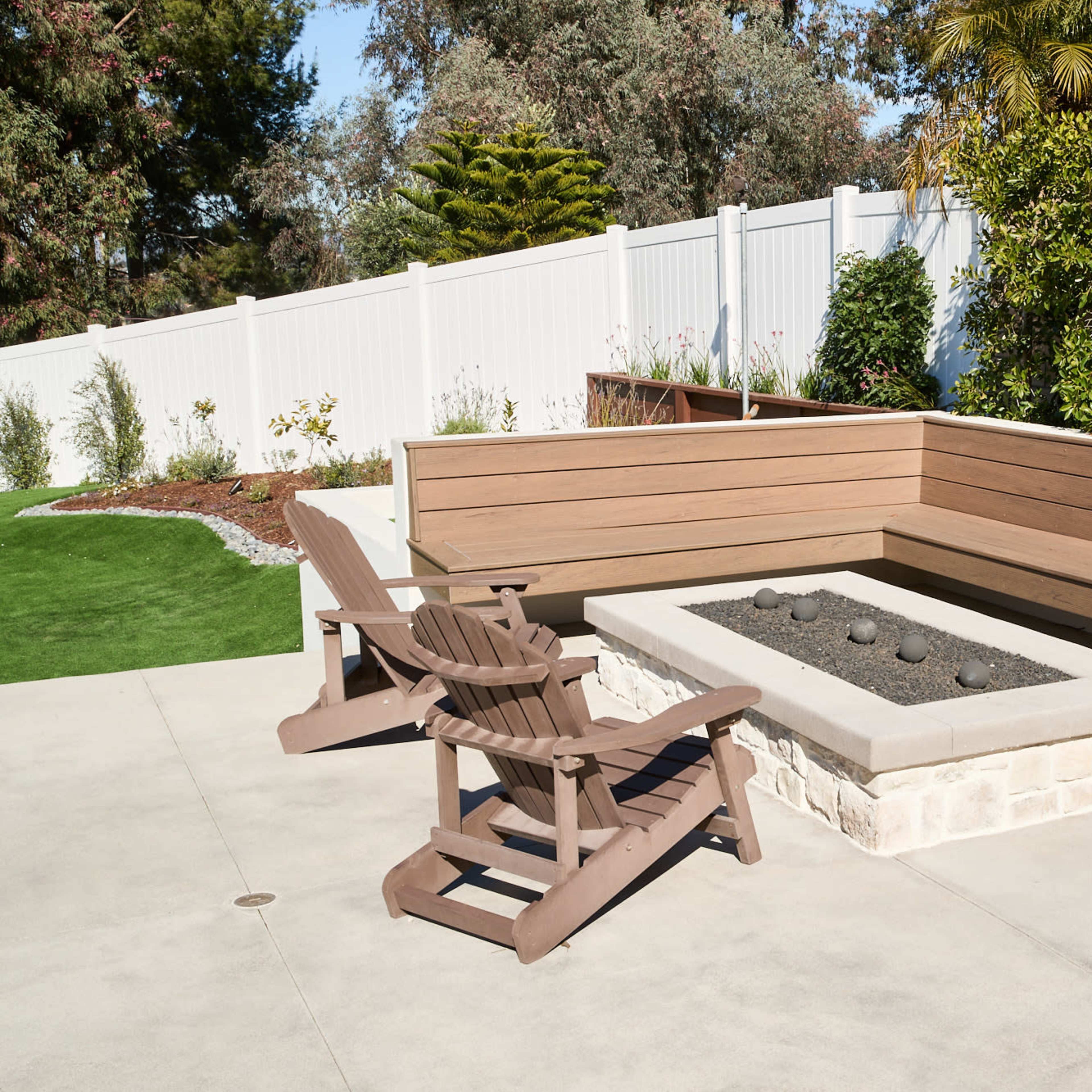 A modern outdoor patio area with a stone fire pit surrounded by wooden seating and two Adirondack chairs.