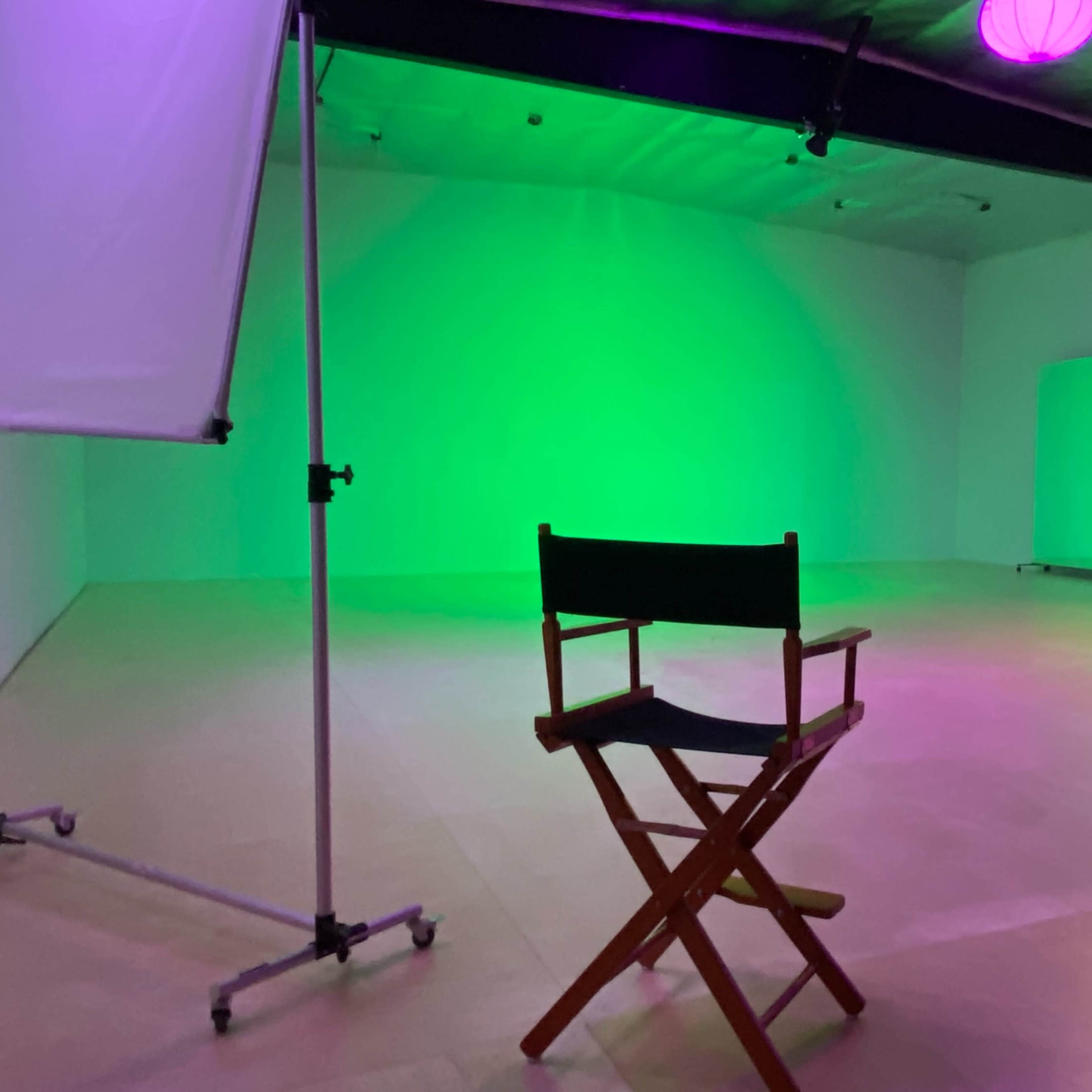 A wooden director's chair is positioned in a green-lit studio with mirrors and minimal furnishings.