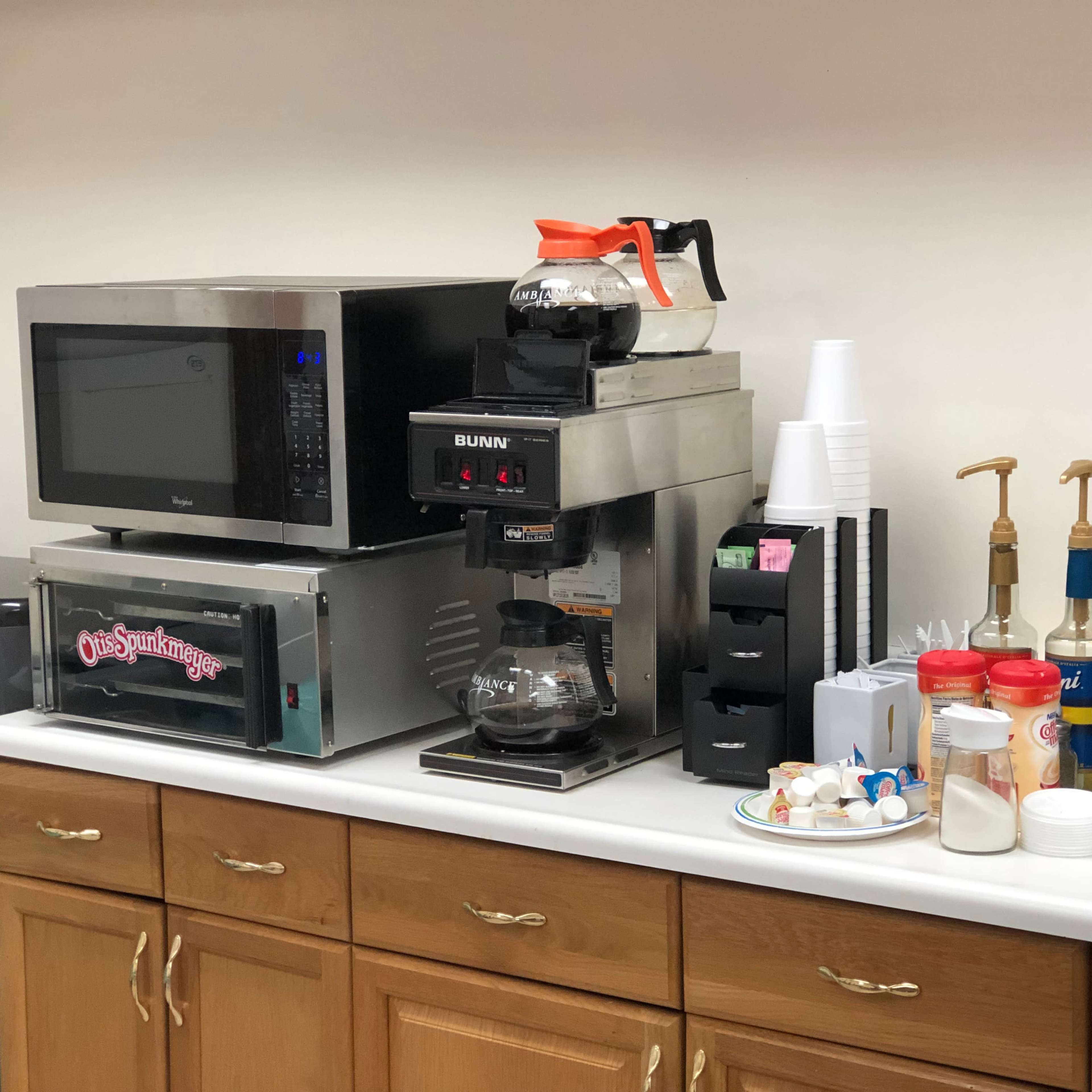 A break room counter with a microwave, coffee maker, and various condiments and utensils.