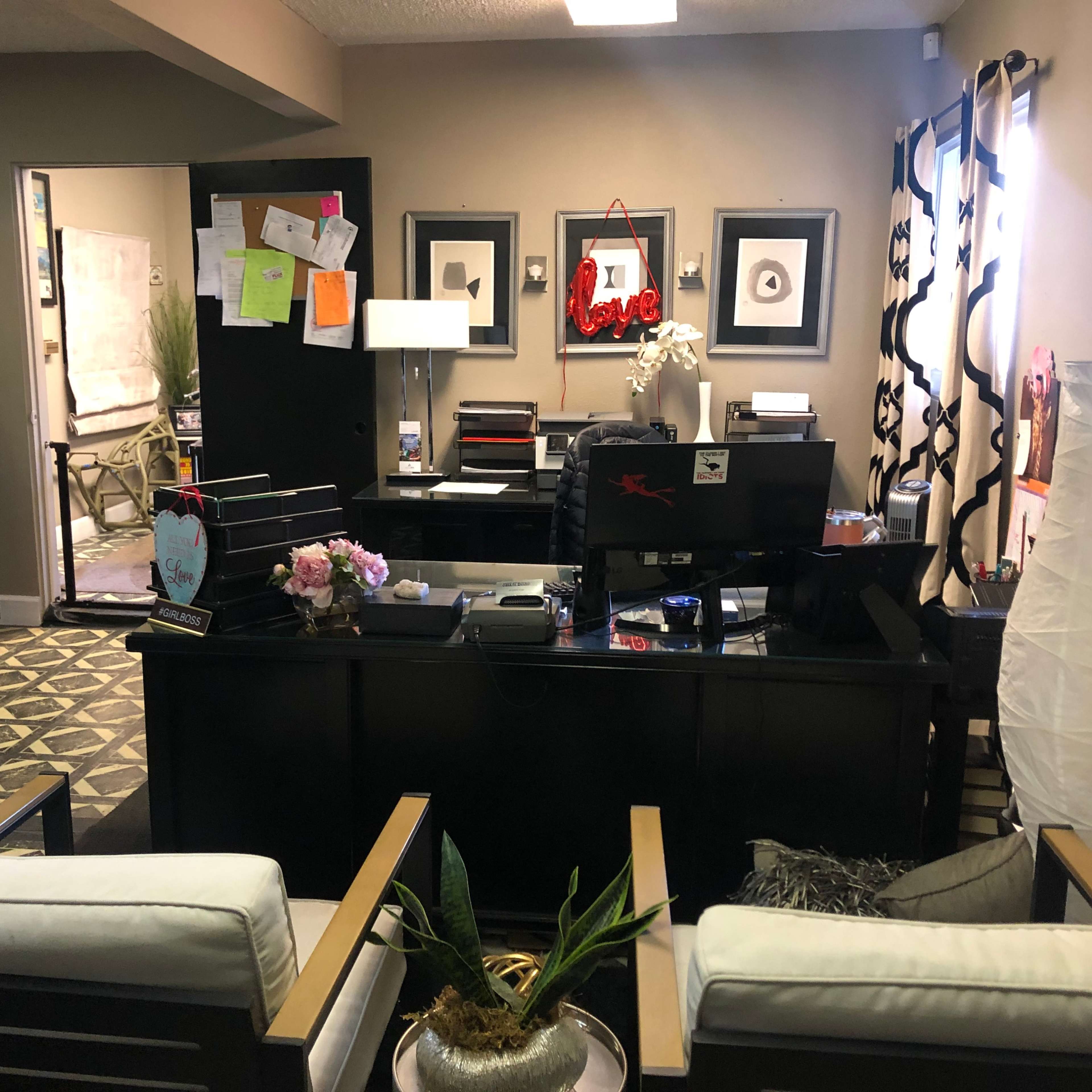 A modern office reception area with a desk, chairs, and decorative items against a backdrop of framed artwork and plants.