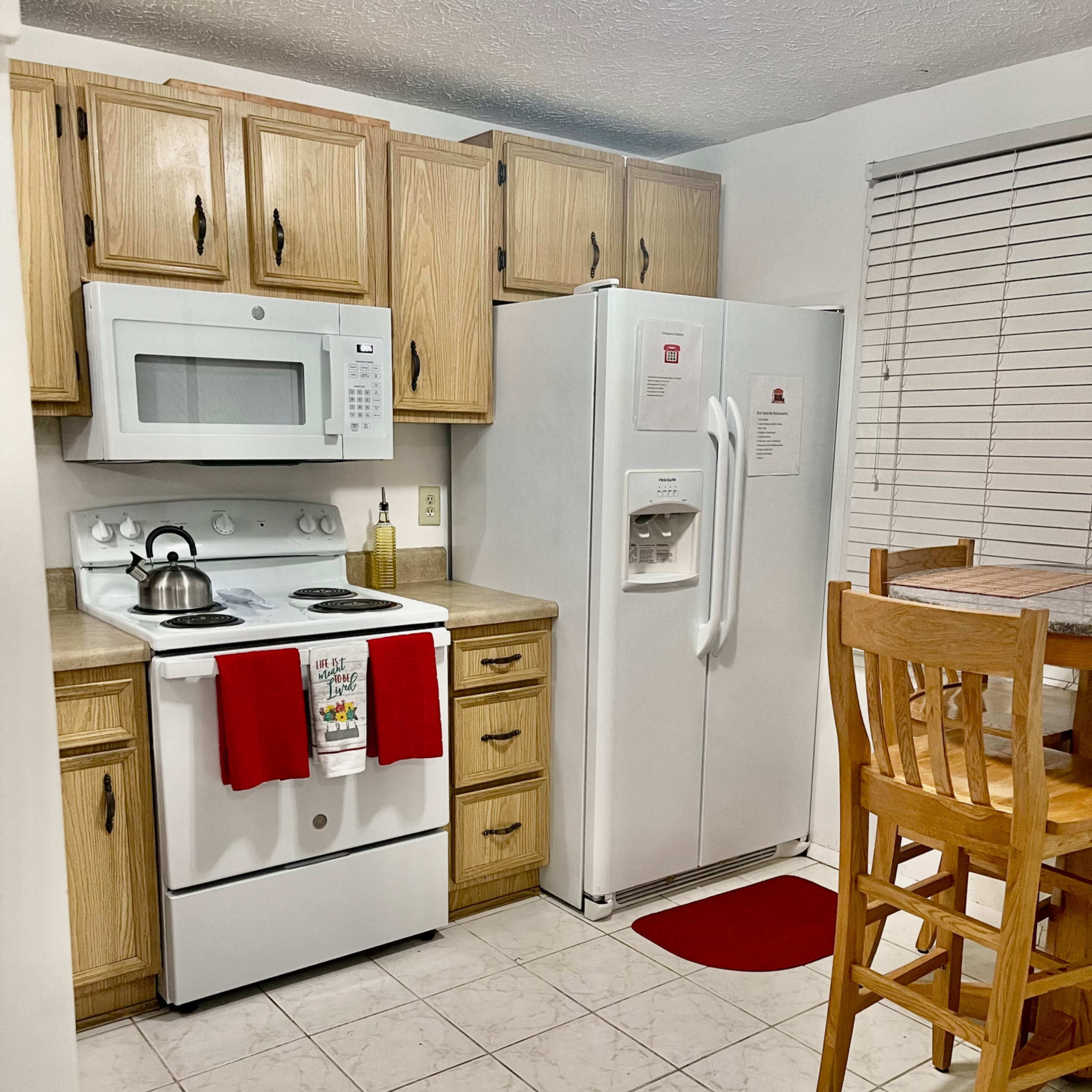 The kitchen features wooden cabinets, a white refrigerator, a stove with a microwave above it, and a small dining table with four wooden chairs.