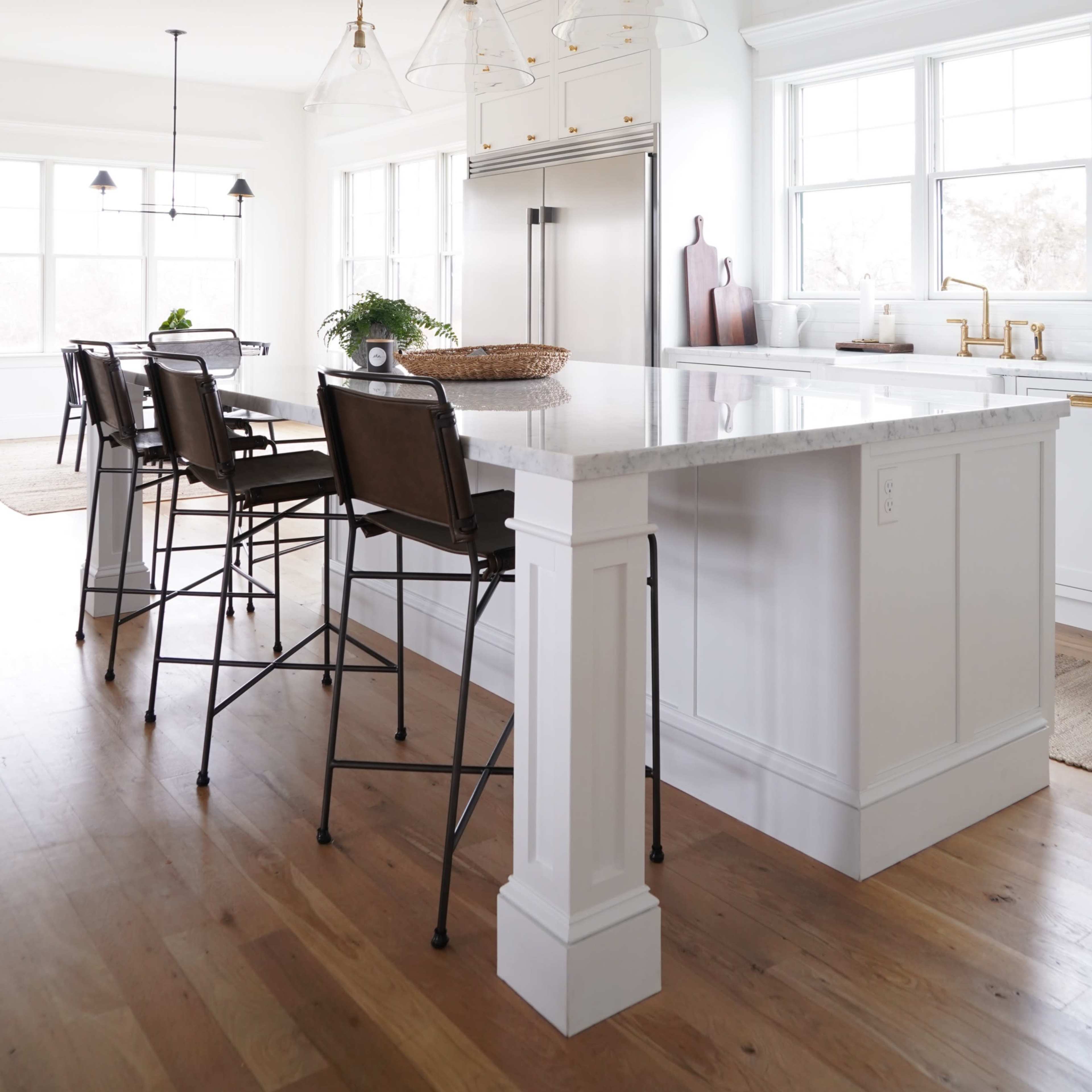 A modern kitchen features a white island with bar stools, gold pendant lights, and stainless steel appliances.