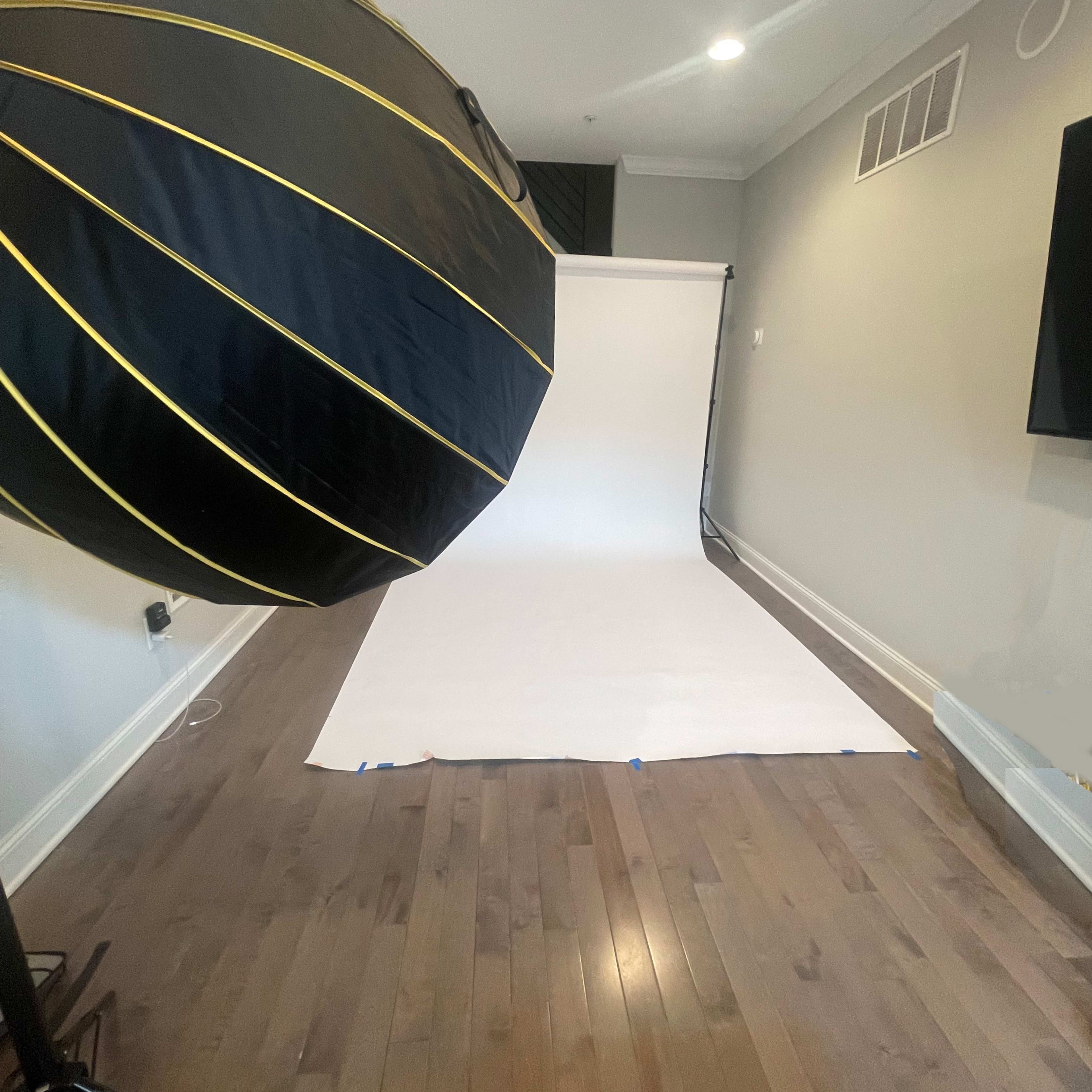 A photography studio setup with a large softbox and a white backdrop on a hardwood floor.