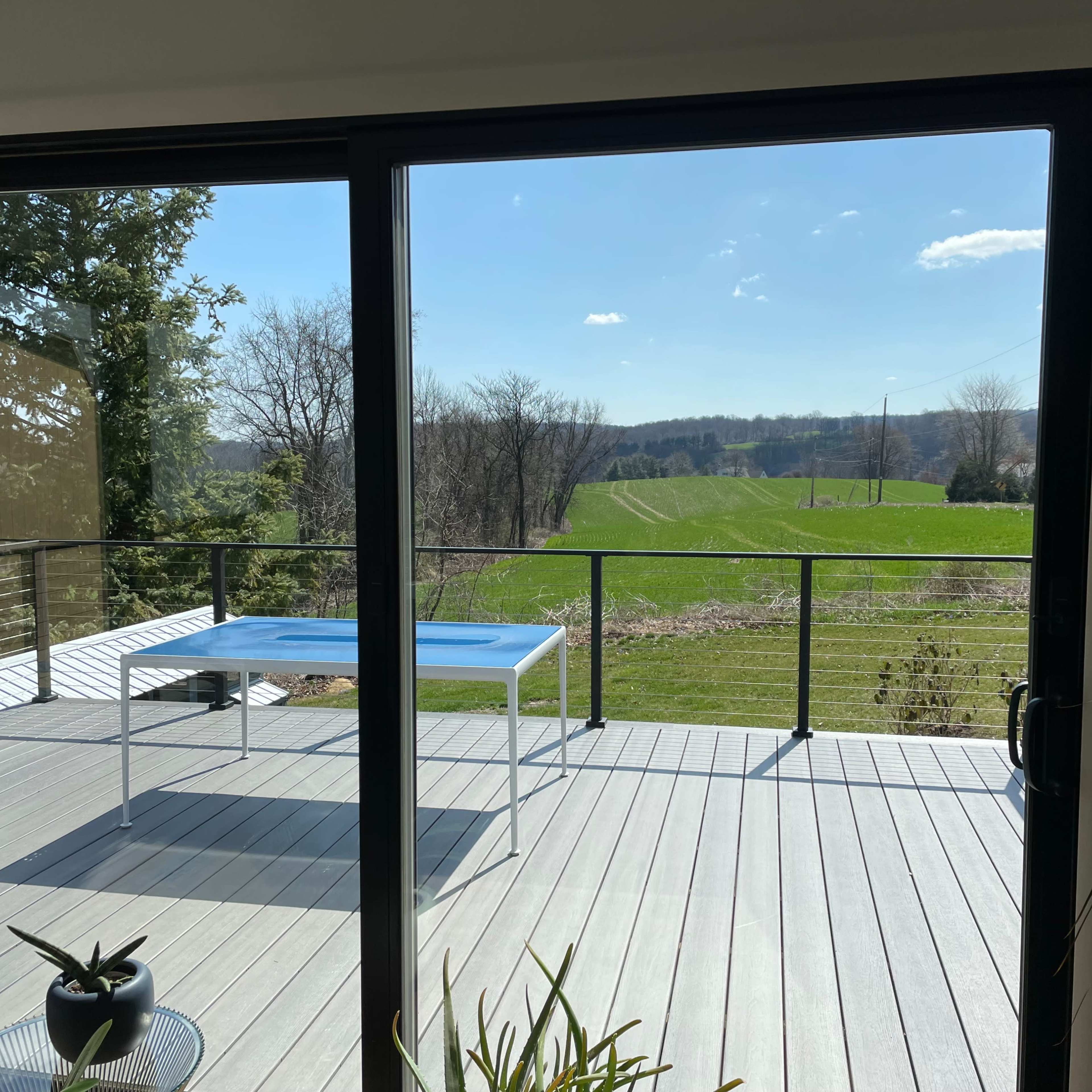 A clear view of a green field is visible through a glass door, framed by a wooden deck and a simple table.