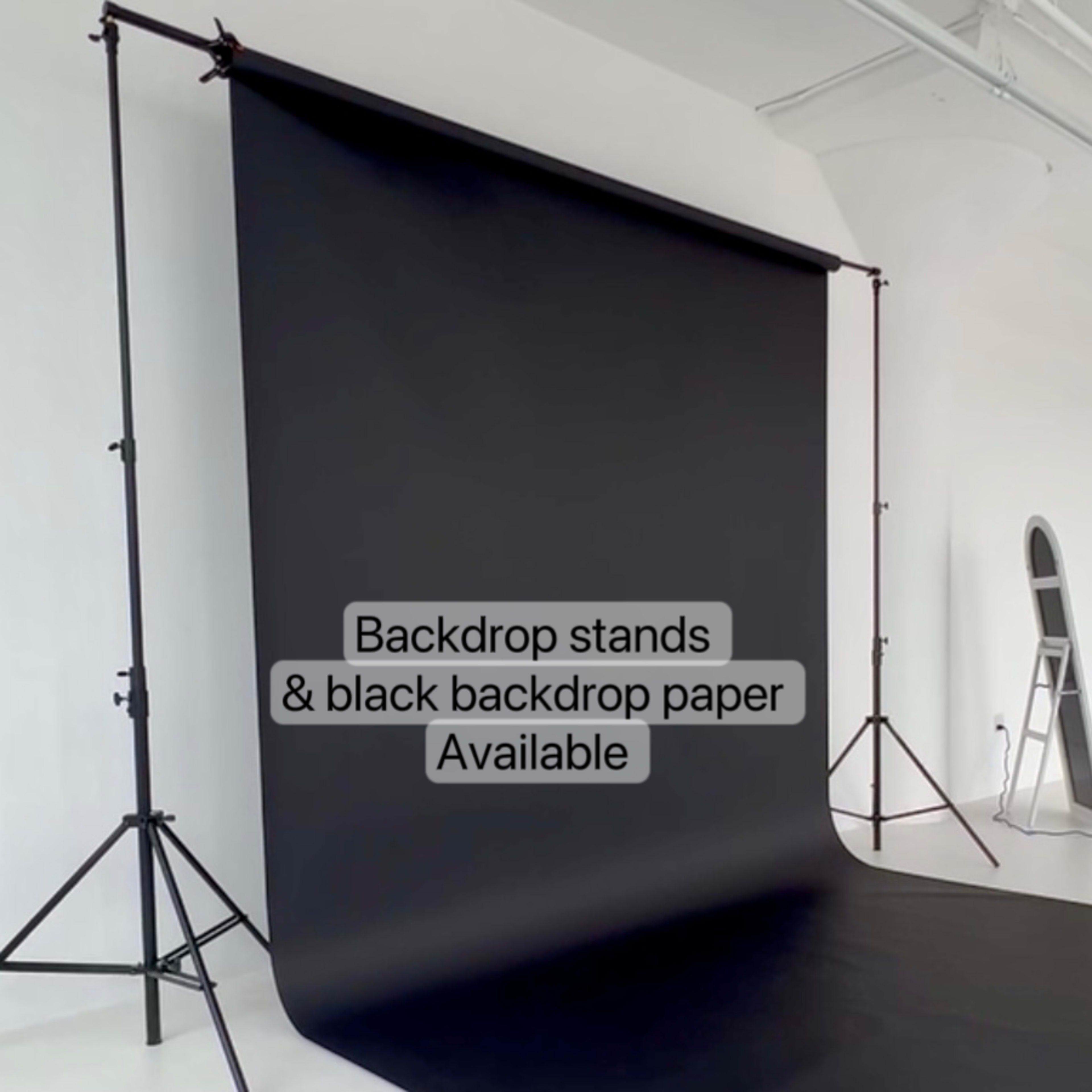 A black backdrop set up on stands in a minimalist studio space with an adjacent mirror and a plant.