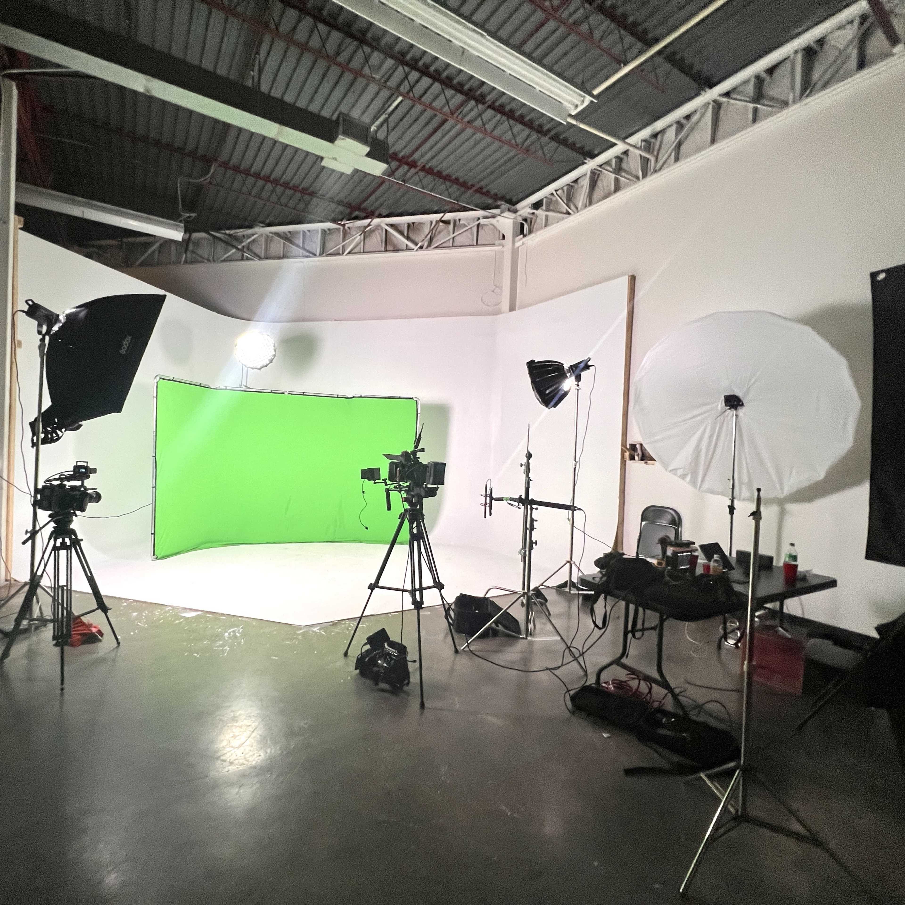 A photography studio setup with multiple cameras, lighting equipment, and a green screen backdrop.