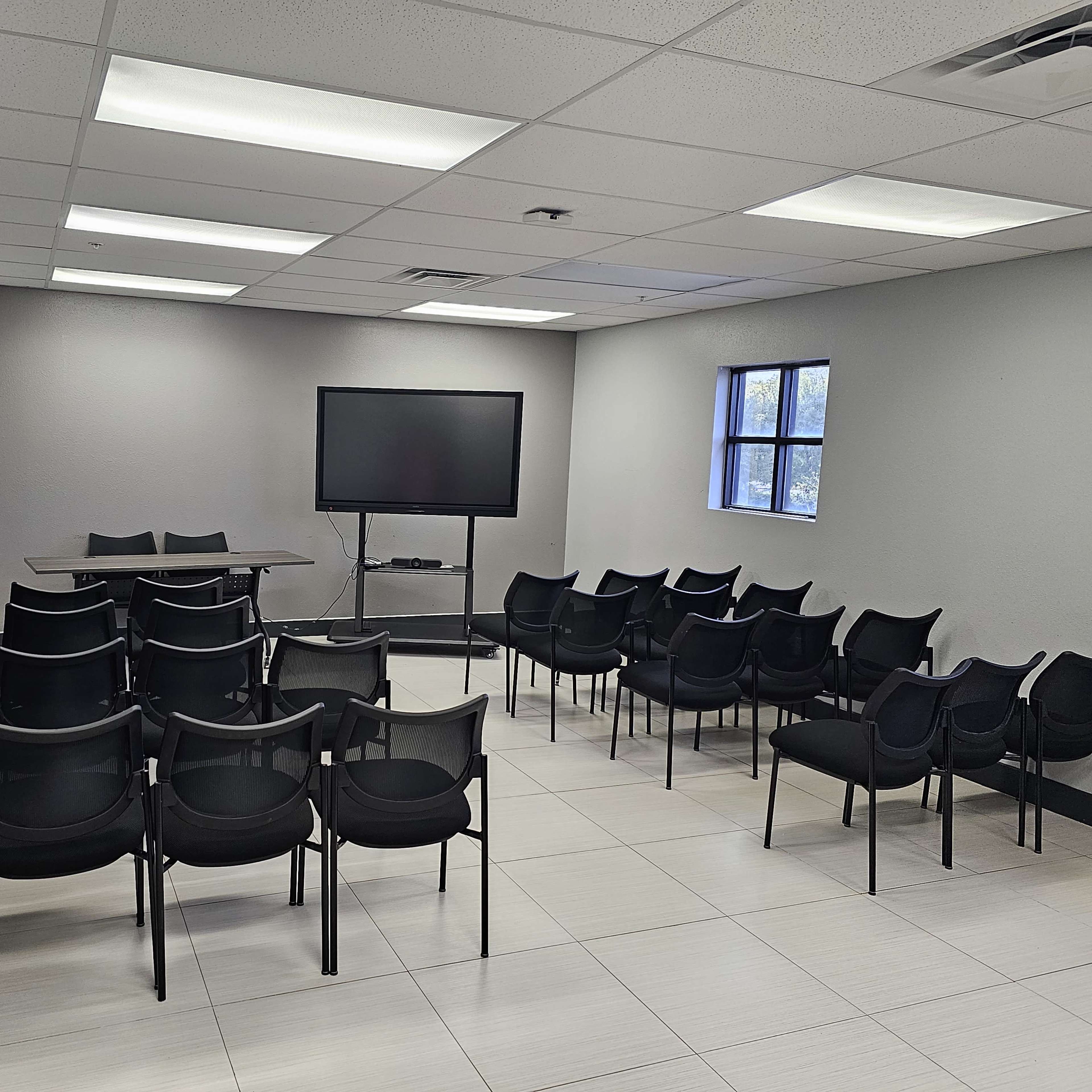 A conference room with a table, a television monitor, and rows of chairs arranged for a meeting.